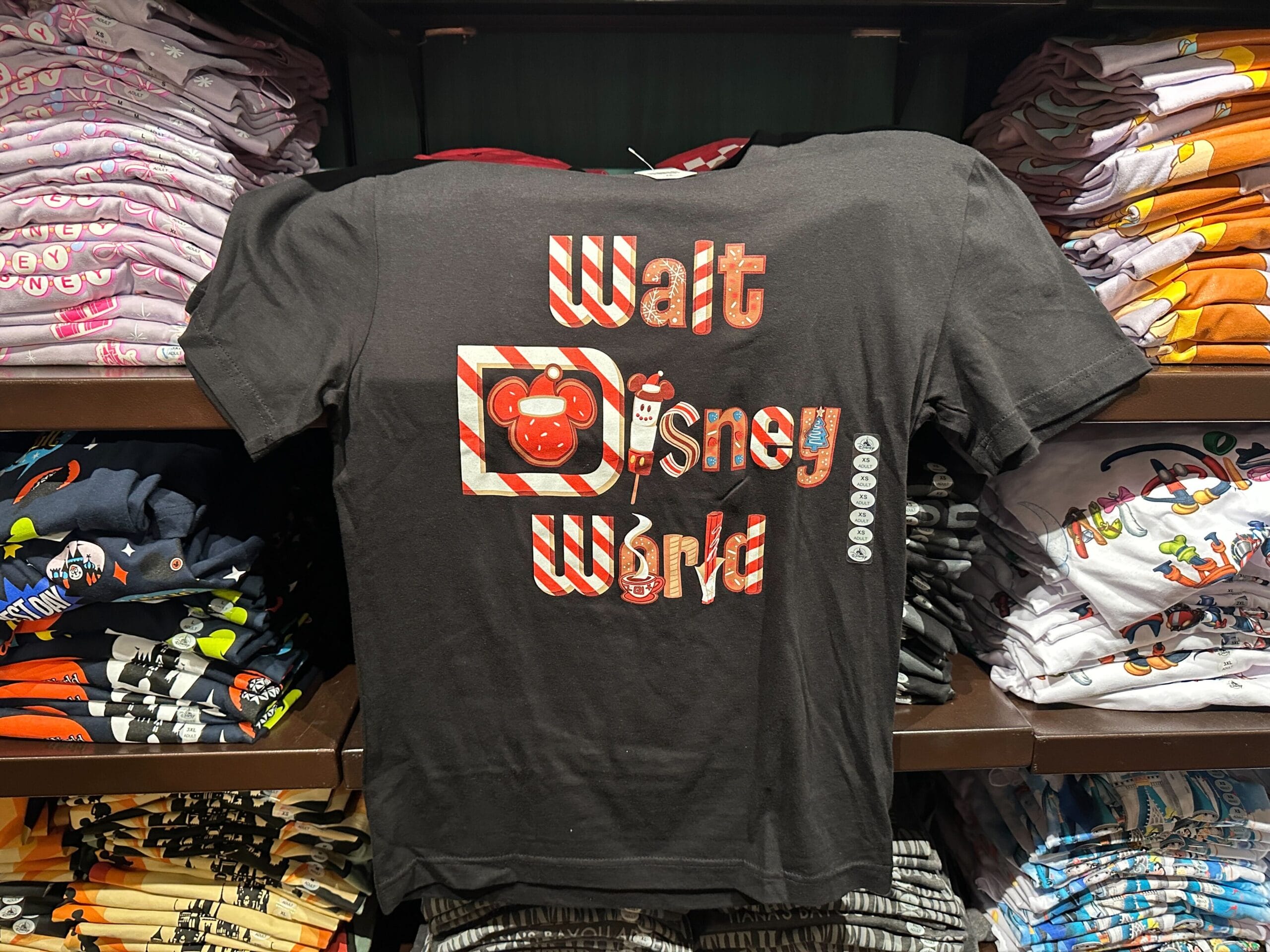 A black Disney World Holiday Shirt with "Walt Disney World" in red and white, displayed among other shirts in a park gift shop.