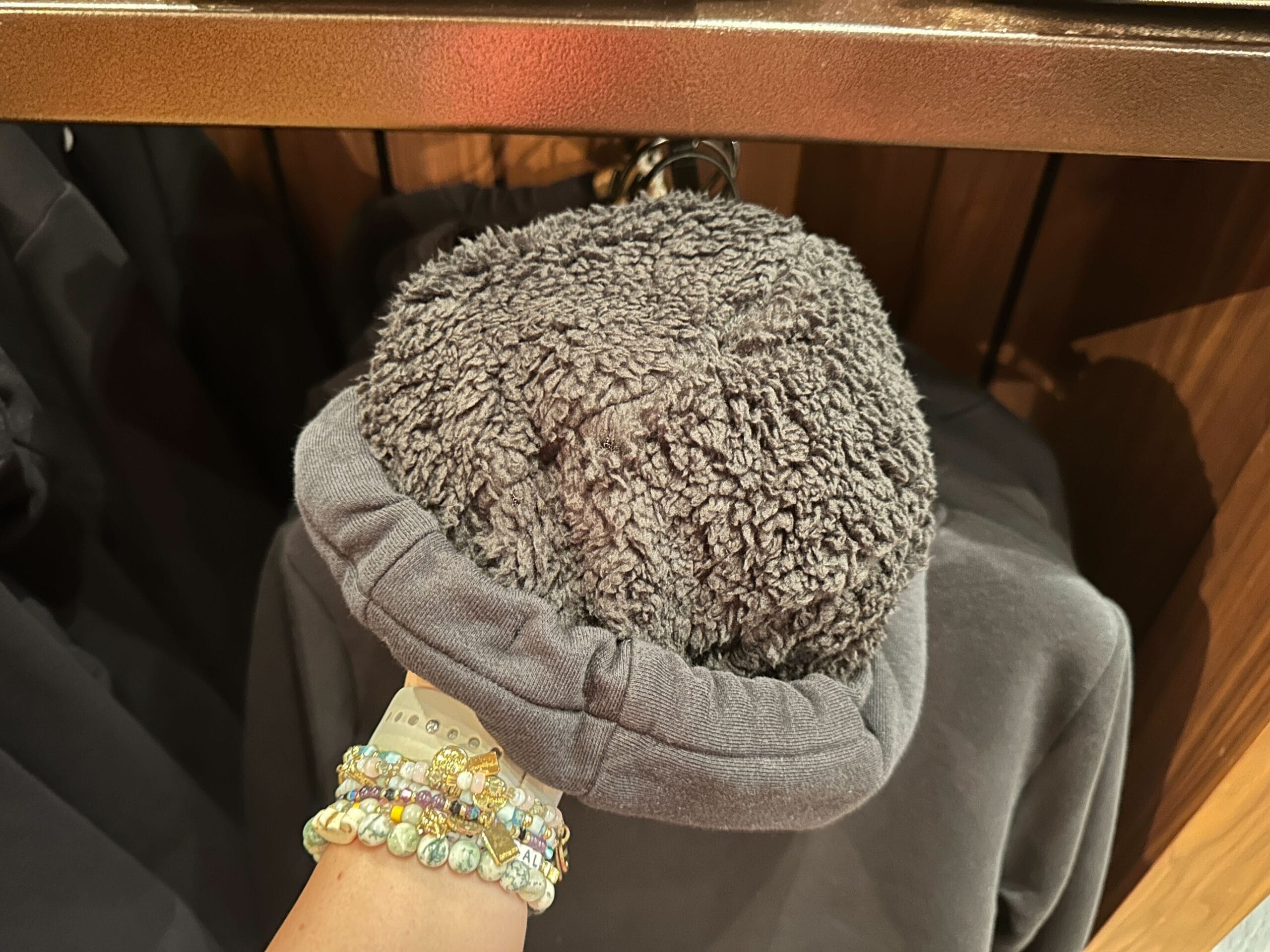 A hand lifts a gray Sherpa hoodie, revealing its soft, fuzzy lining—perfect for staying cozy while strolling through Disney parks.