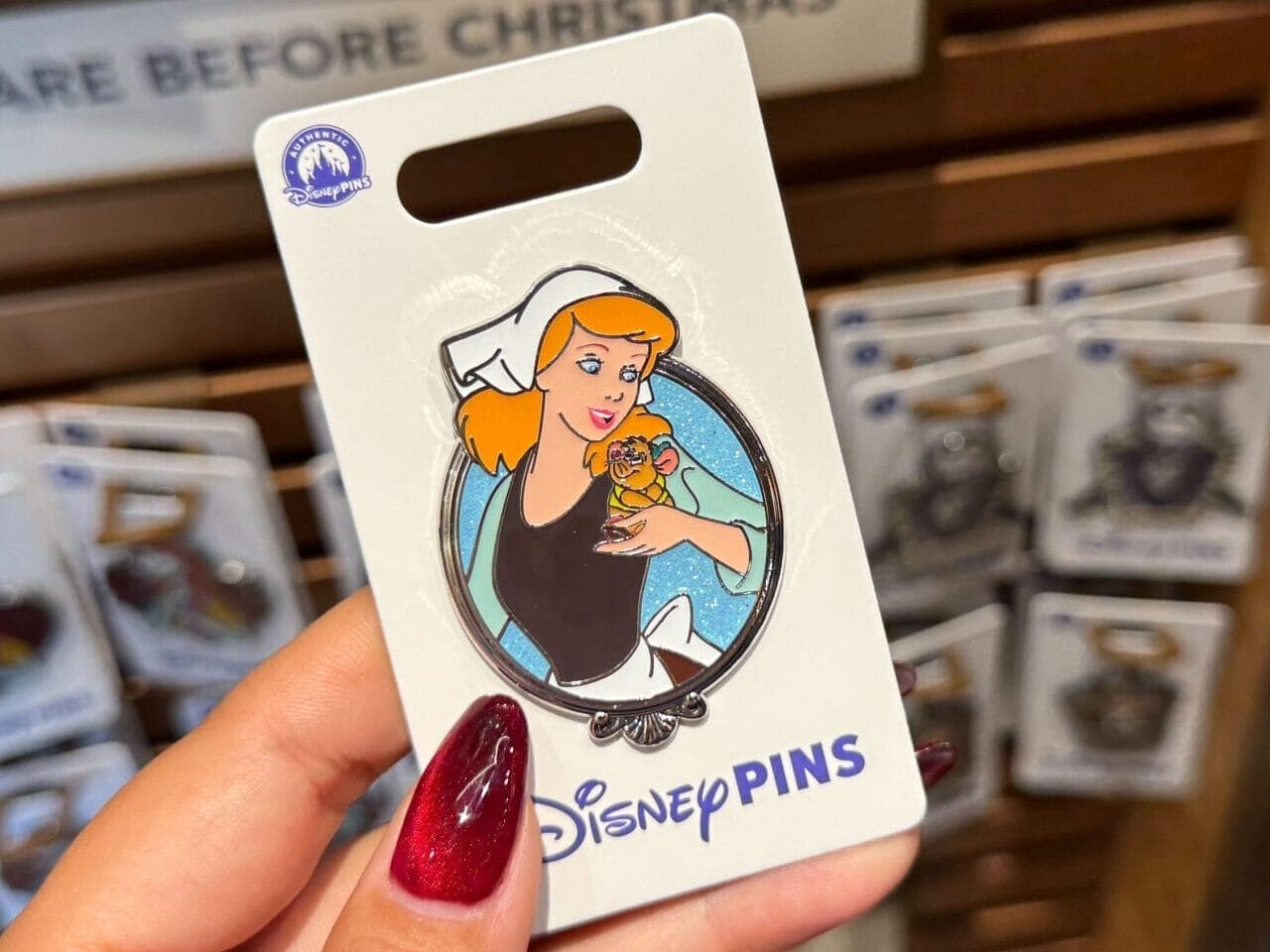 A hand displays a Cinderella Disney Princess pin with a backdrop of assorted Disney pins, like those sold at Disney Parks worldwide.