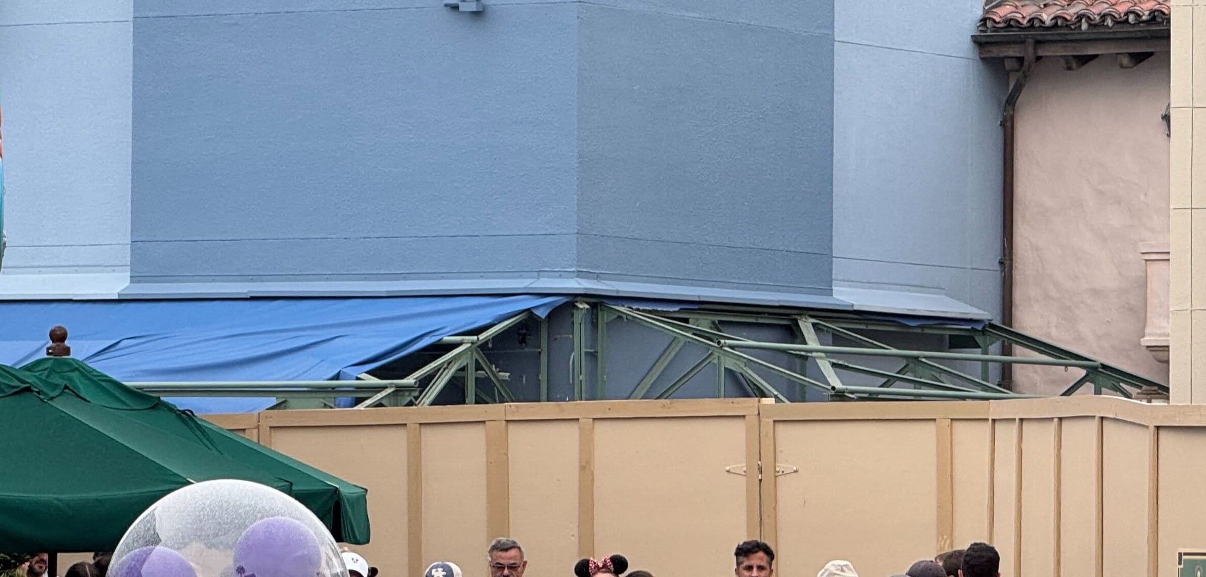 Hollywood Studios construction site with blue tarp and green beams, likely Animation Courtyard demo; crowd watching, no castle visible.
