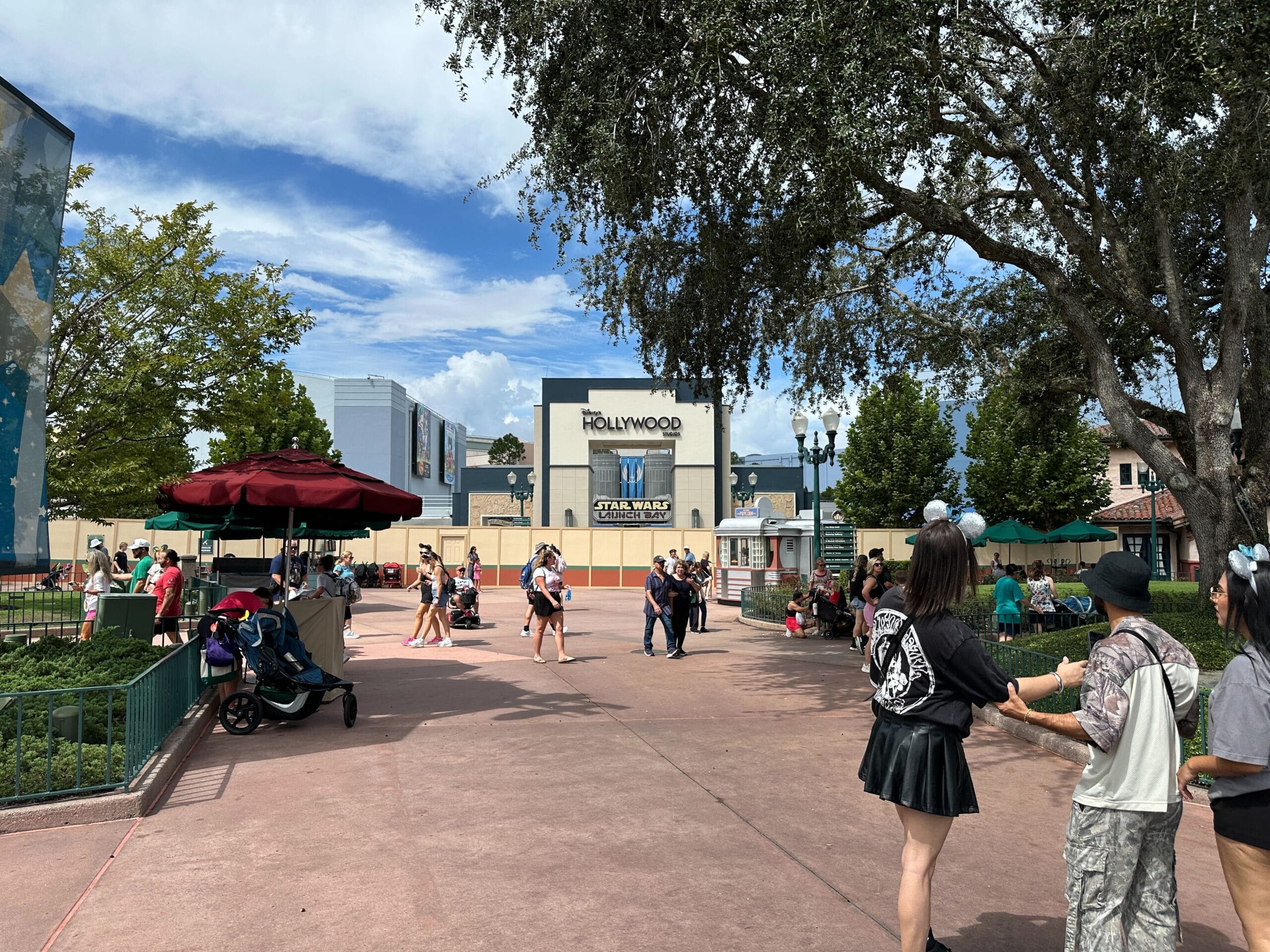 Guests mingle in the sunlit plaza by the Animation Courtyard sign at Disney's Hollywood Studios, construction walls in view nearby.