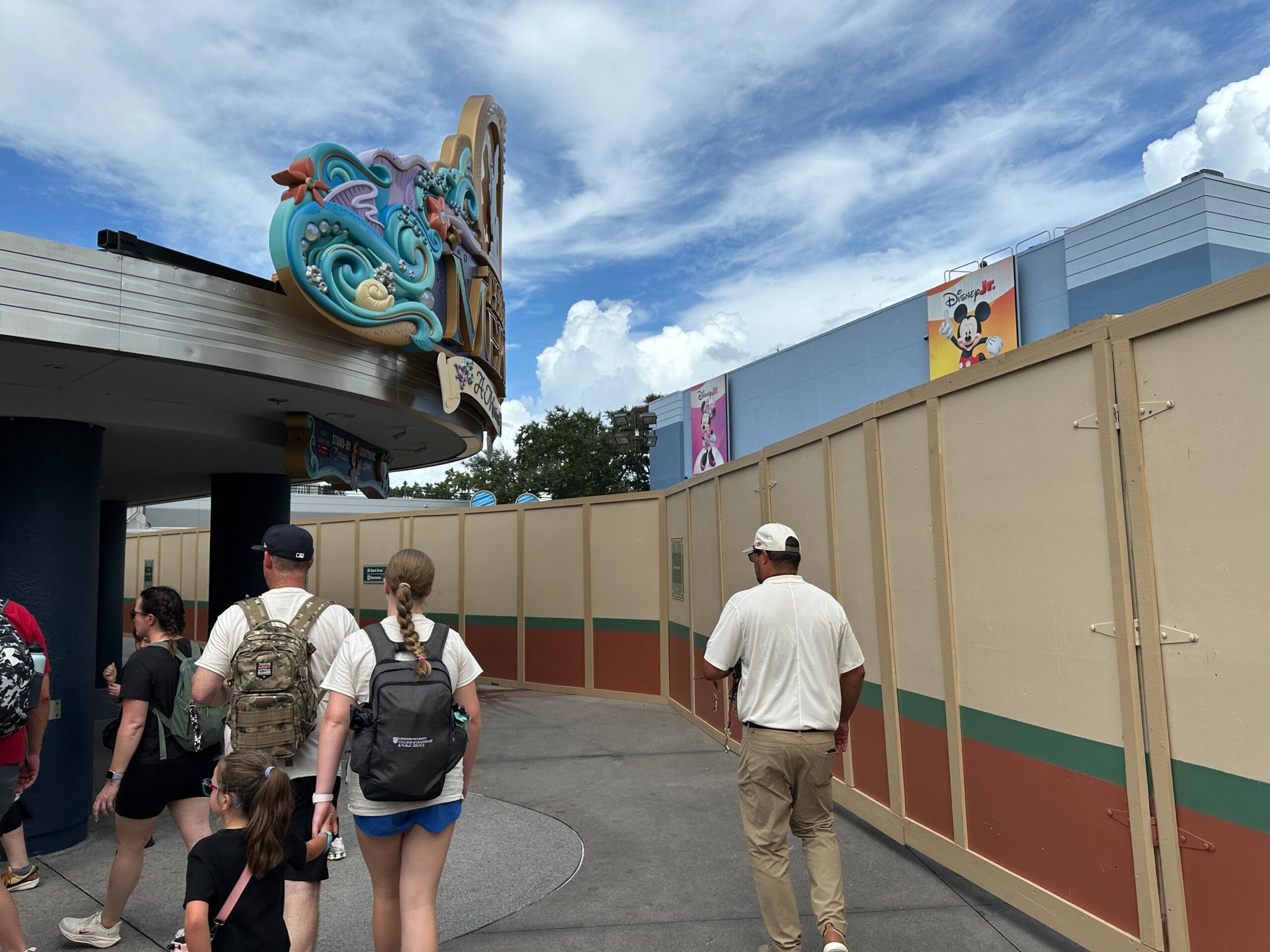 Guests walk by construction walls in Animation Courtyard at Hollywood Studios, with colorful cartoon posters lining the background.