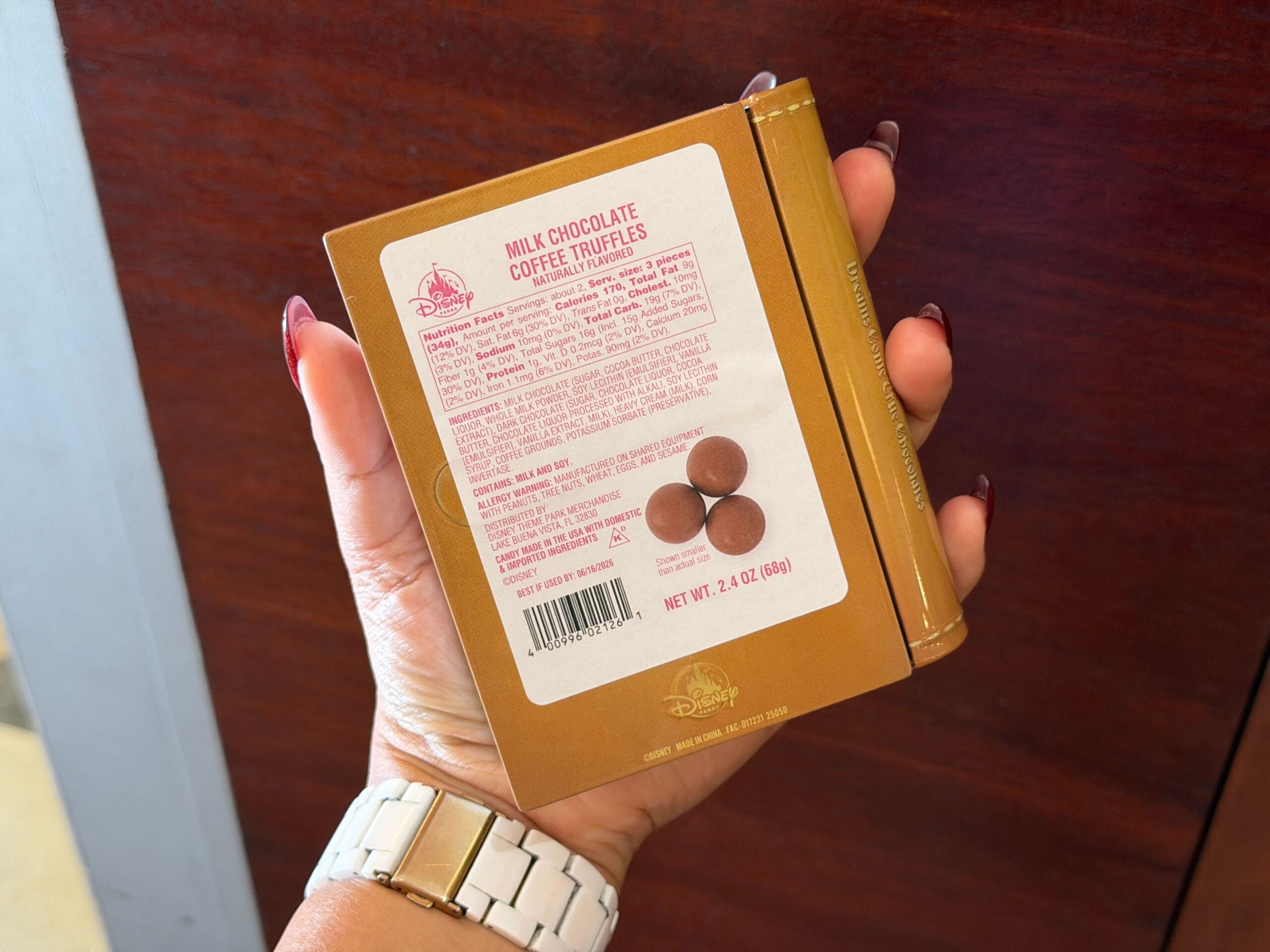 A hand displays a Disney chocolate treat box, perfect as a Disney Parks souvenir, set against a wooden surface background.
