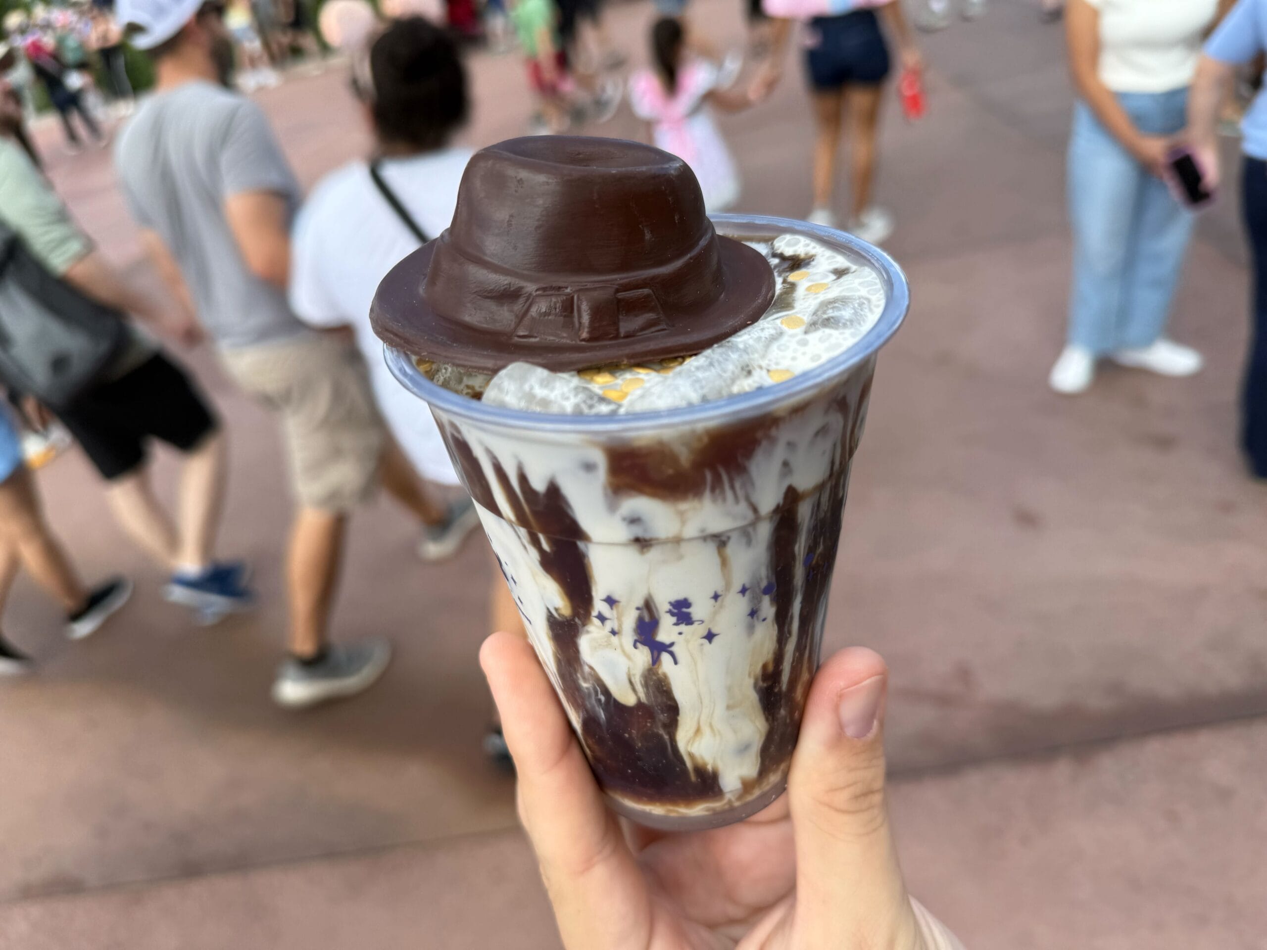 A hand holds a cold brew coffee drink topped with a chocolate fedora at Disney's Hollywood Studios.
