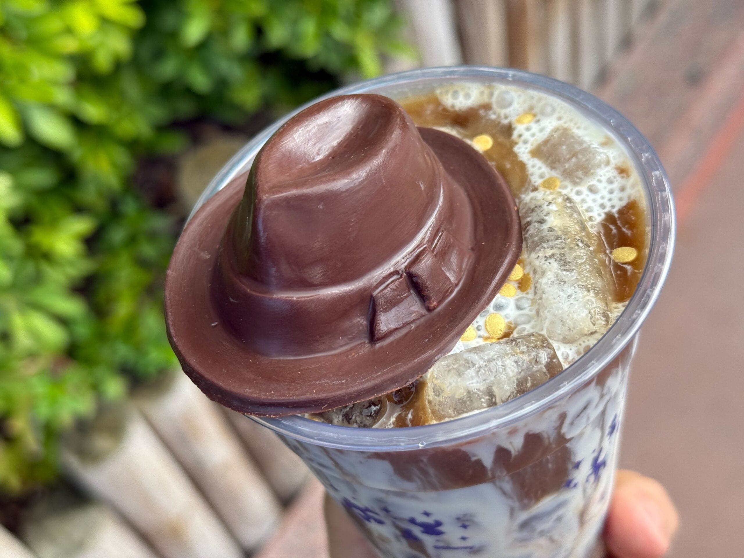 Epic Cold Brew with milk and a chocolate fedora, sipped outside among lush plants at Disney's Hollywood Studios in Florida.