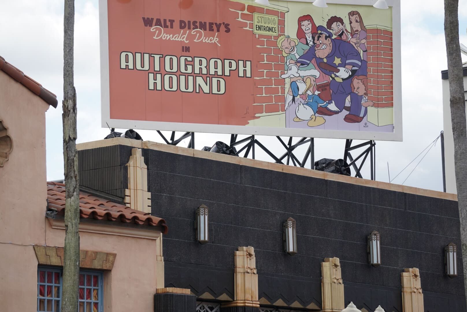 A billboard in Disney's Hollywood Studios promotes "Donald Duck in Autograph Hound" beside a brick wall—no castle in view.