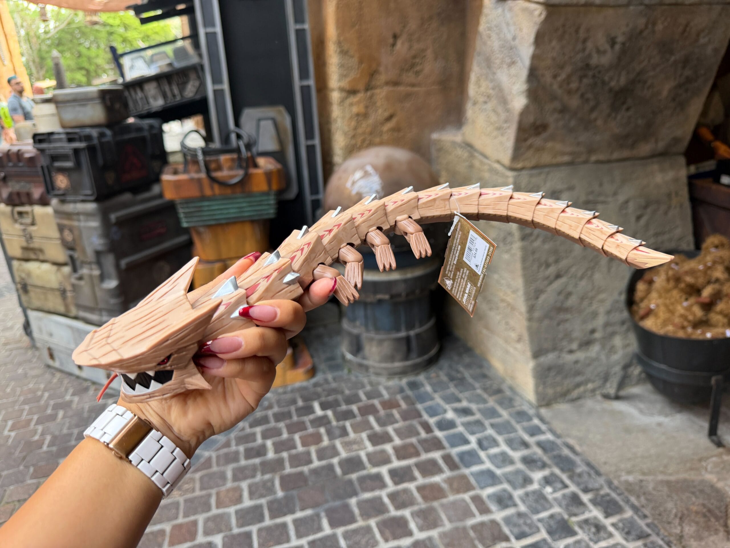 A hand displays a Krayt Dragon Toys model outdoors by crates and stone walls, evoking the Star Wars: Galaxy’s Edge in Disney parks.