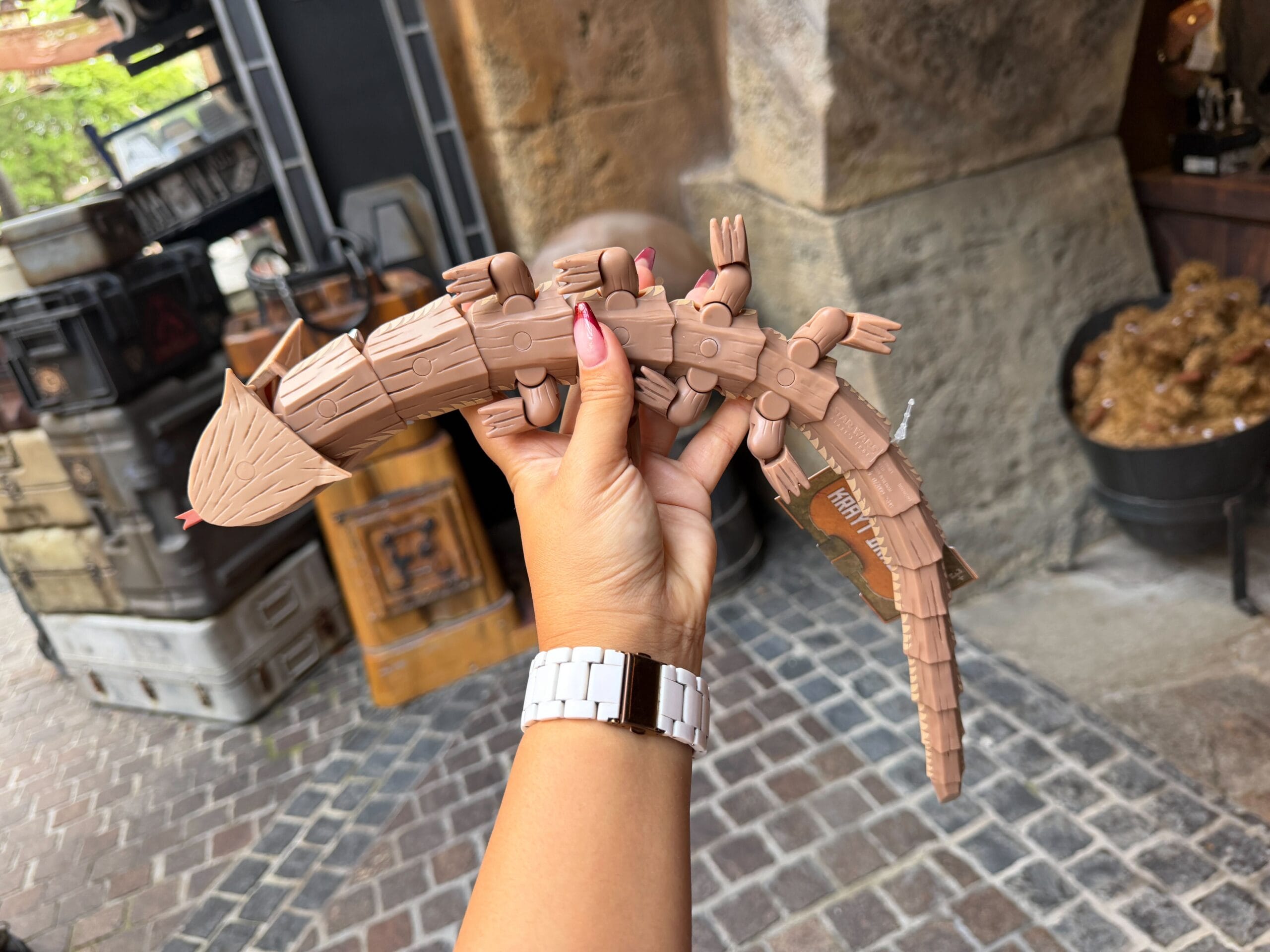 A hand displays a segmented brown Krayt Dragon toy with forked tongue at Galaxy's Edge, Walt Disney World’s Star Wars-themed market.