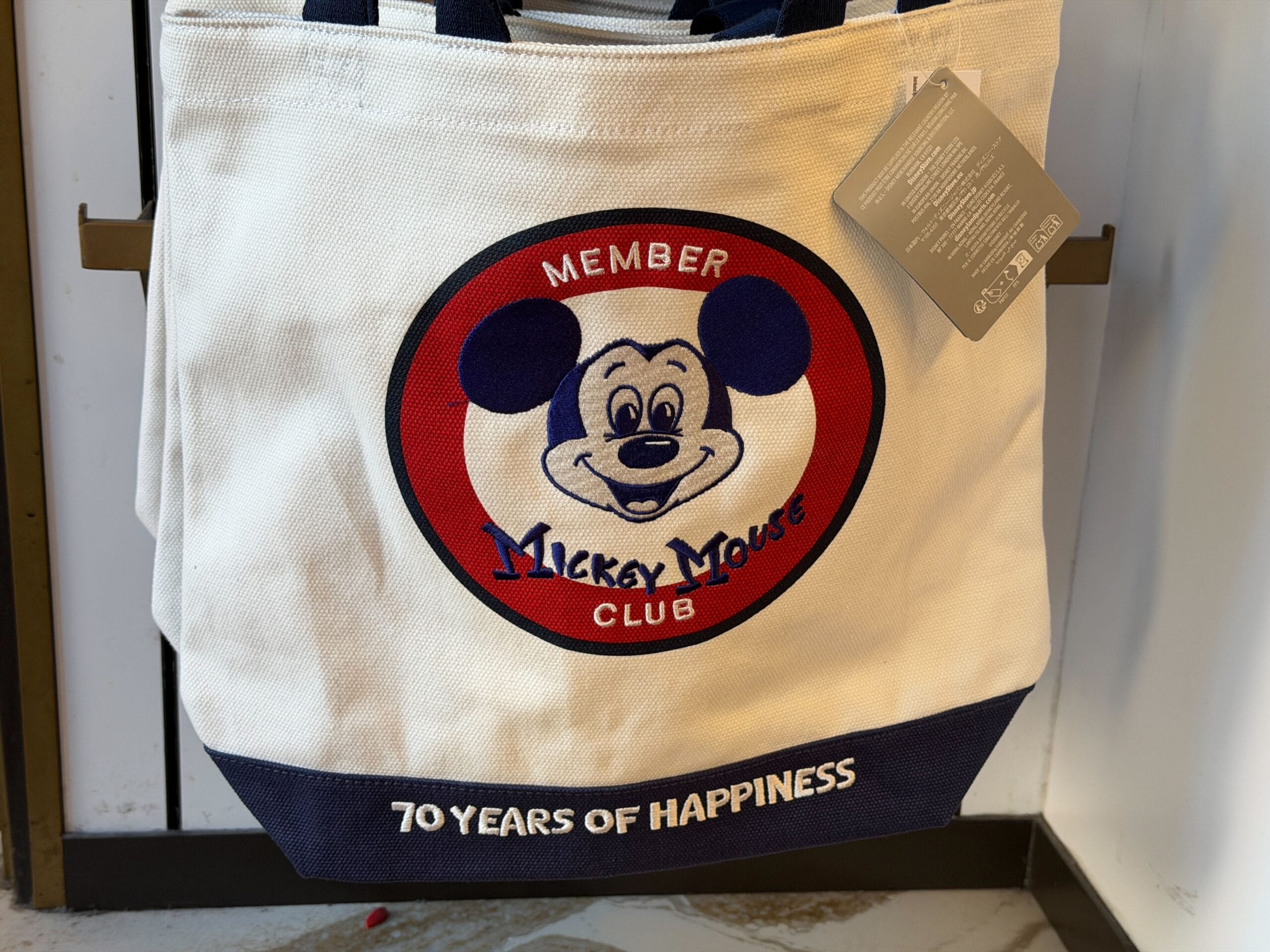 White tote bag featuring the classic Mickey Mouse Club logo and "70 Years of Happiness," a nod to Disney theme park nostalgia.