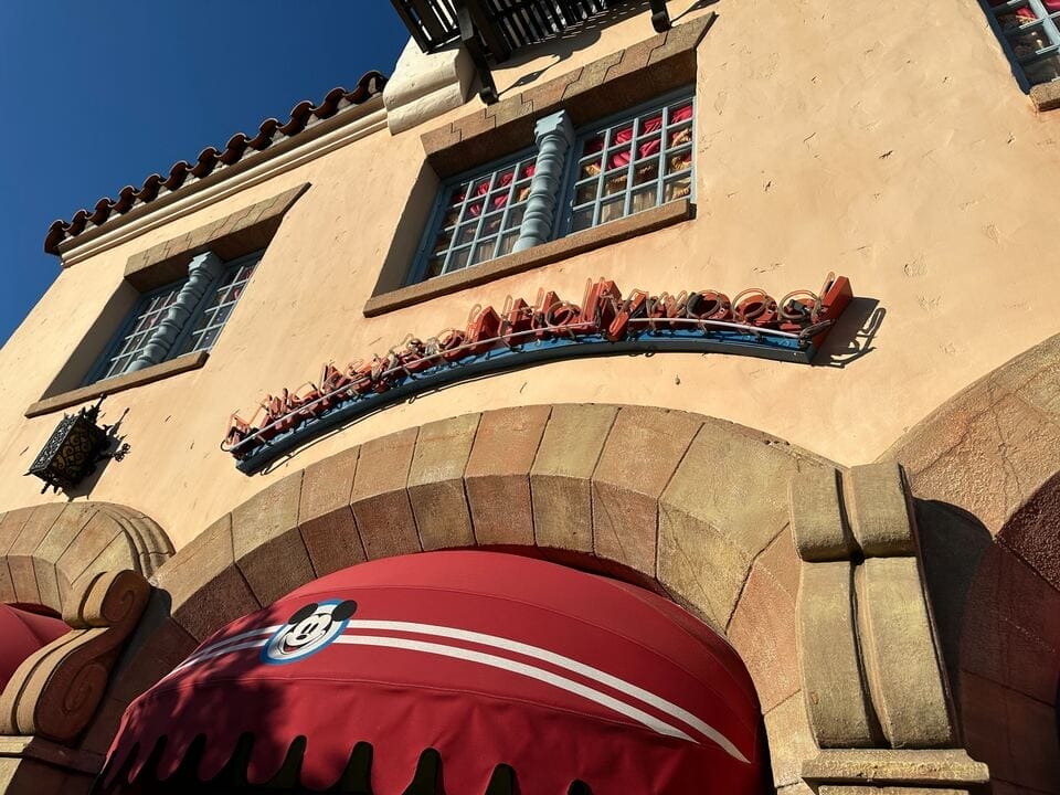 Spanish-style shop with a red arched awning, neon signage, and Wishes T-shirts at the entrance—clear Walt Disney World vibes.