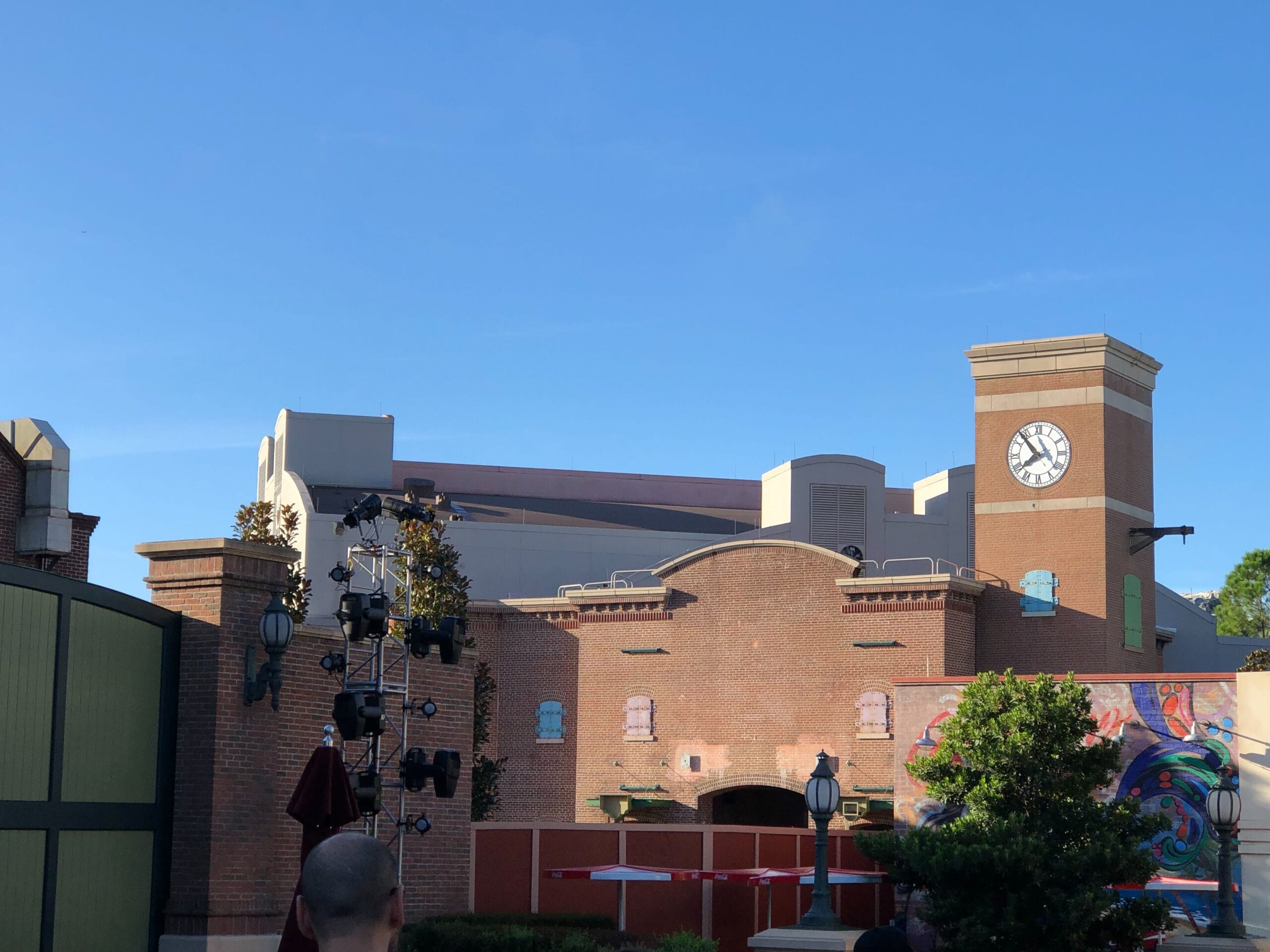 A brick building with a clock tower and marquee, resembling MuppetVision 3D at Disney’s Hollywood Studios, under a clear blue sky.