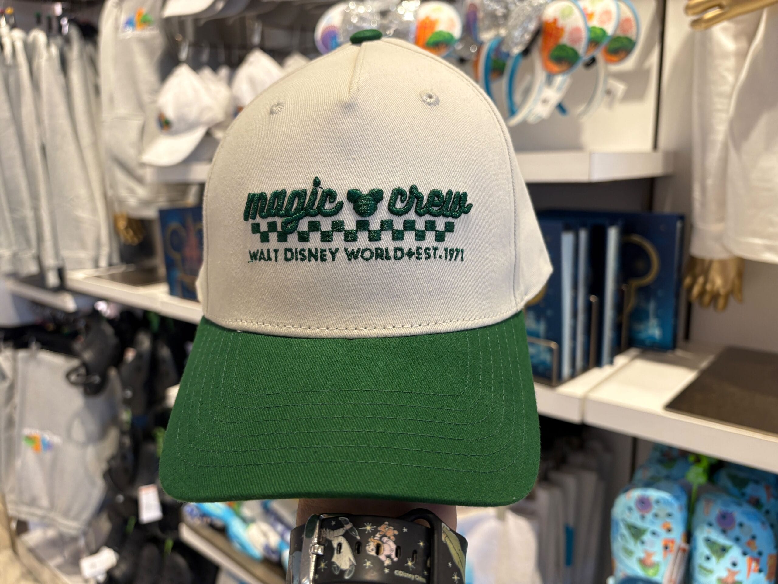 A beige and green "Magic Crew Walt Disney World Est. 1971" hat on display amid Disney Parks merch, evoking classic WDW style.