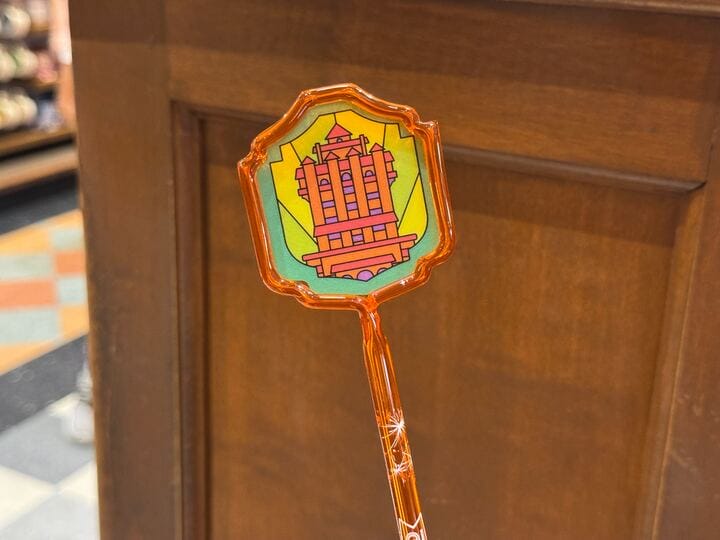 An orange plastic wand with a vibrant image of the Hollywood Tower Hotel, resembling the iconic Disney park attraction, on wood.