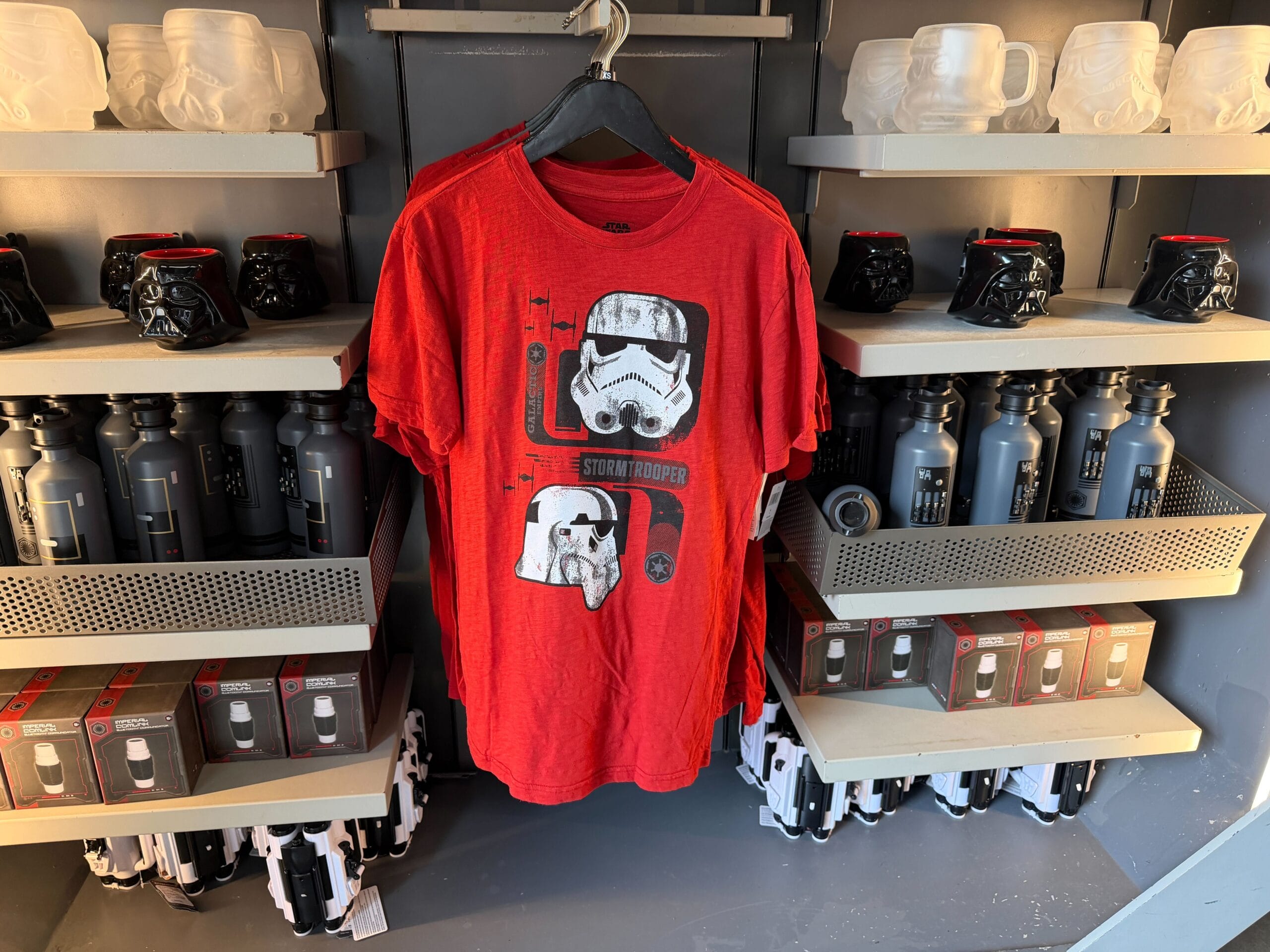 Red Stormtrooper t-shirt on a rack, flanked by Star Wars mugs and bottles—classic Disney Parks merch shop display.
