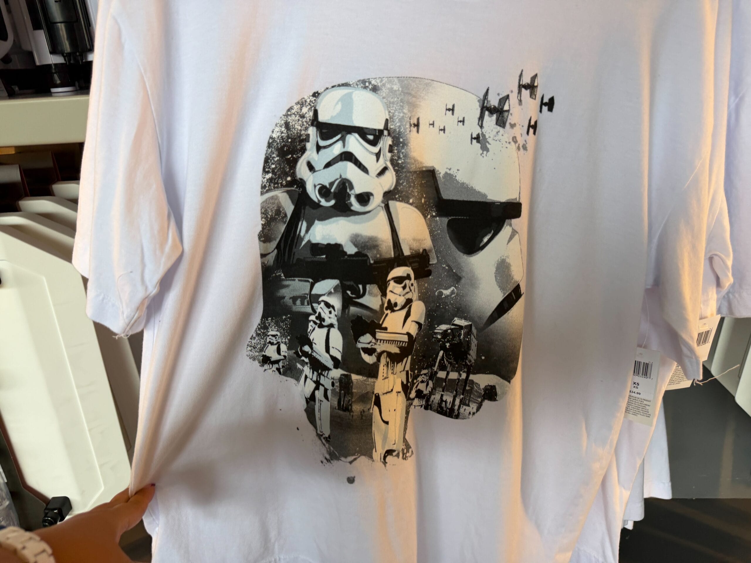 White T-shirt with black and white Star Wars Stormtrooper, TIE fighters, and characters, reminiscent of Disney park Star Wars merch.
