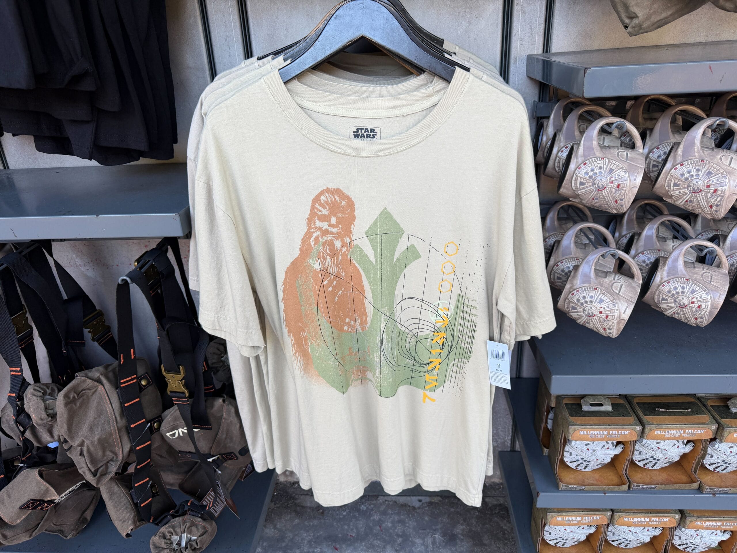 Beige Star Wars t-shirt featuring Chewbacca, hanging on a store rack at a Disney park, surrounded by themed merchandise.