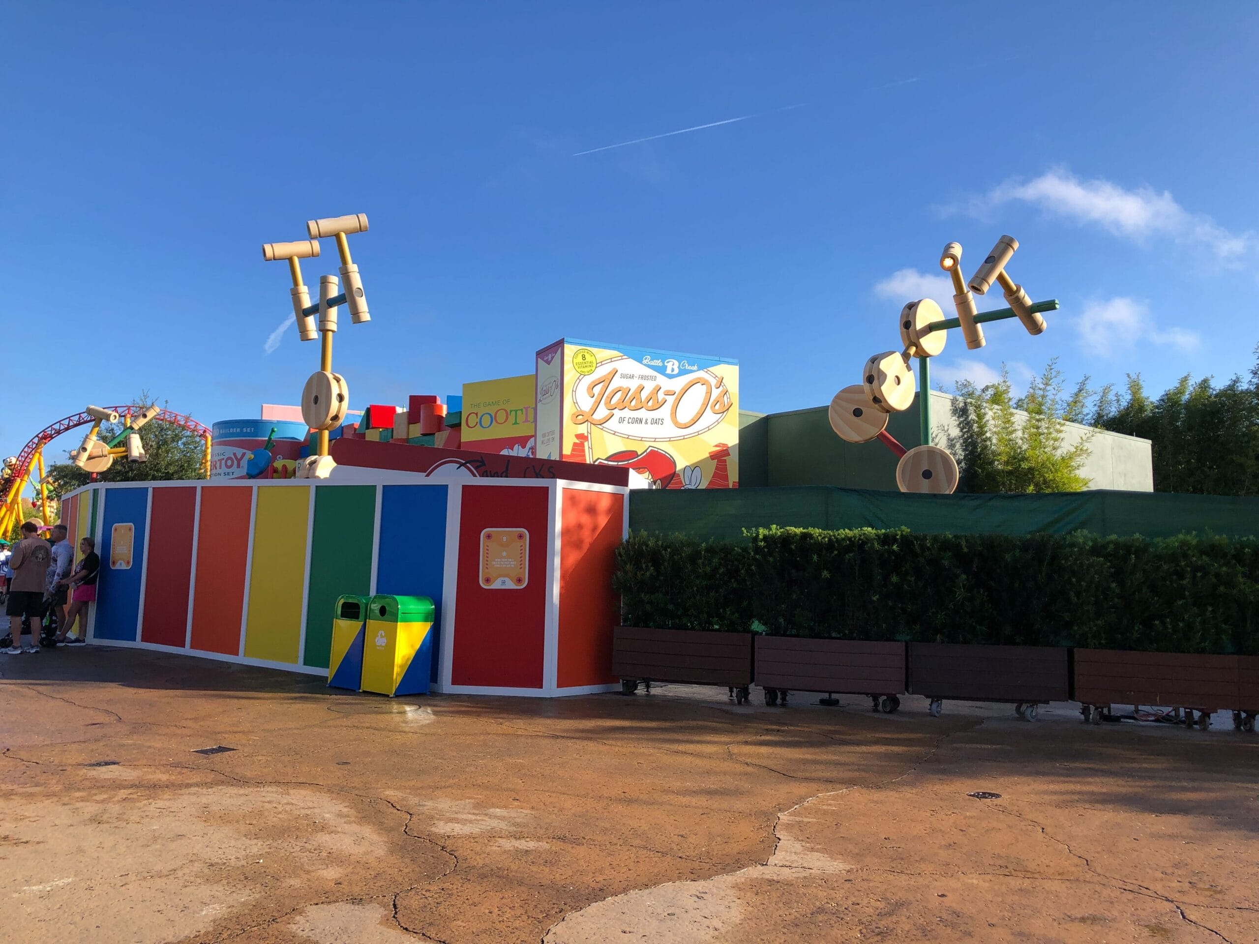 Vibrant Toy Story Land construction wall and oversized Tinkertoy sculptures by a snack kiosk, blue sky above, no castle in view.