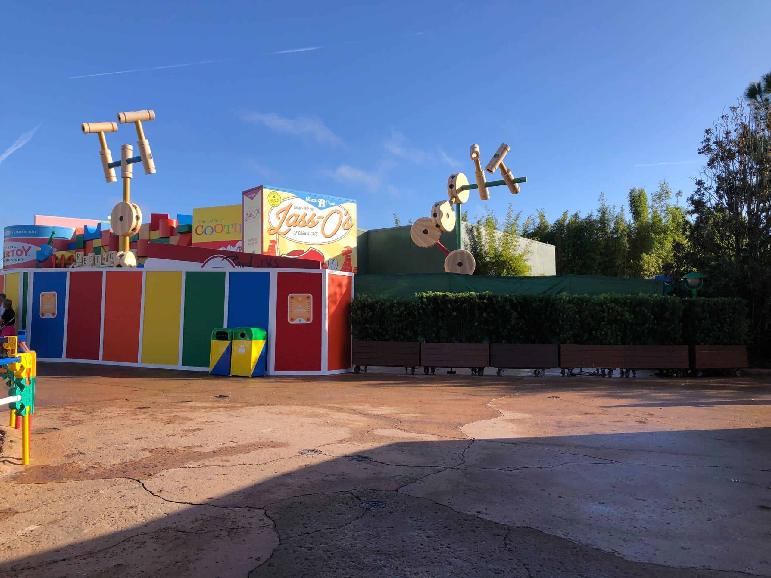Toy Story Land in a Disney park, featuring bright walls, Tinkertoy decor, benches, and a snack kiosk under sunny skies. No castle visible.