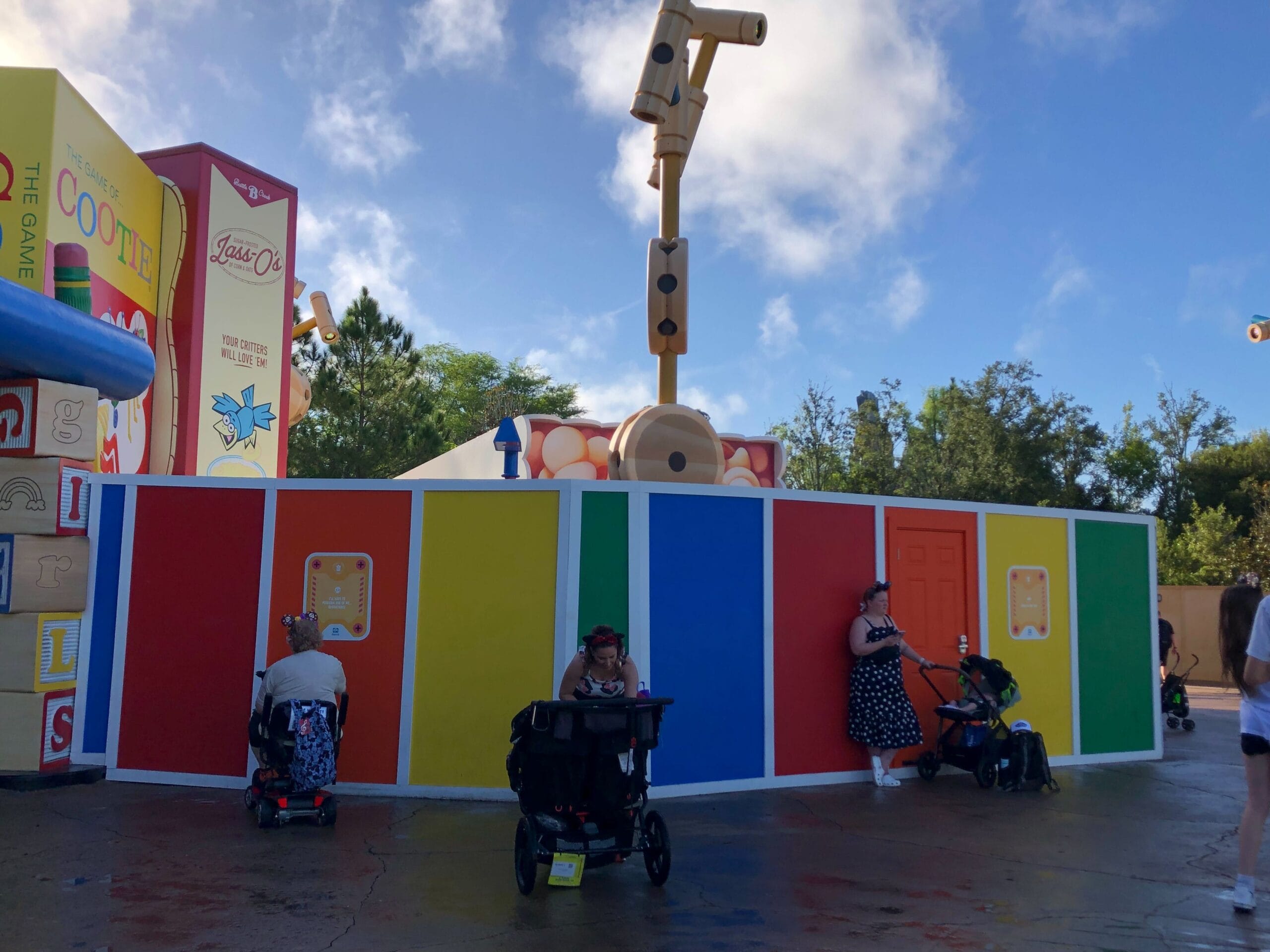 Bright construction wall and snack kiosk at Toy Story Land in a Disney park, with visitors, strollers, and a partly cloudy sky.