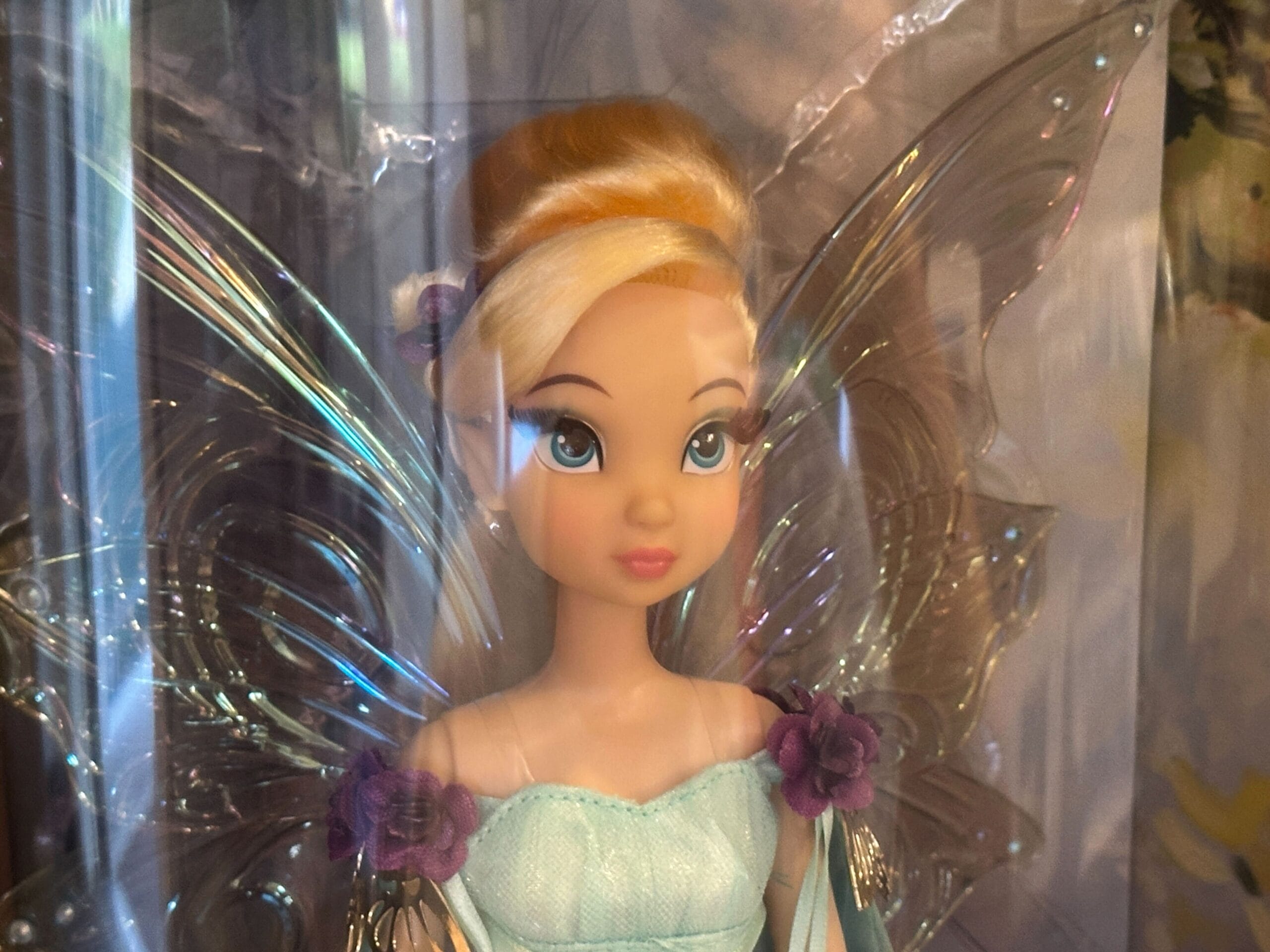 A Designer Tinker Bell fairy doll, inspired by Disney Parks, with blonde hair, blue eyes, glittery wings, and a green dress with purple flowers.
