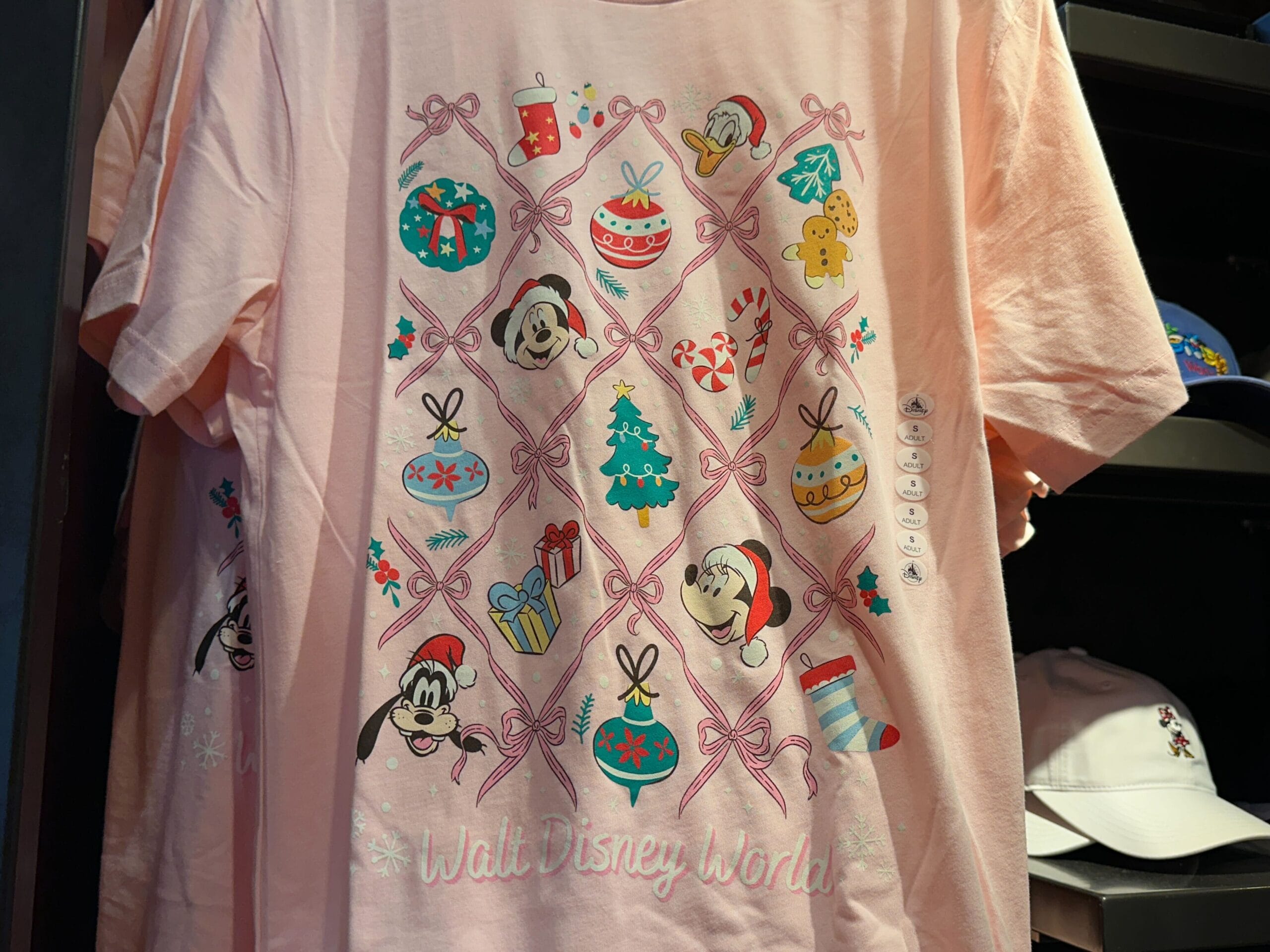 Festive pink Disney World holiday tee with Christmas decor, cartoon Mickey, Minnie, and Goofy—a design unique to Disney World parks.
