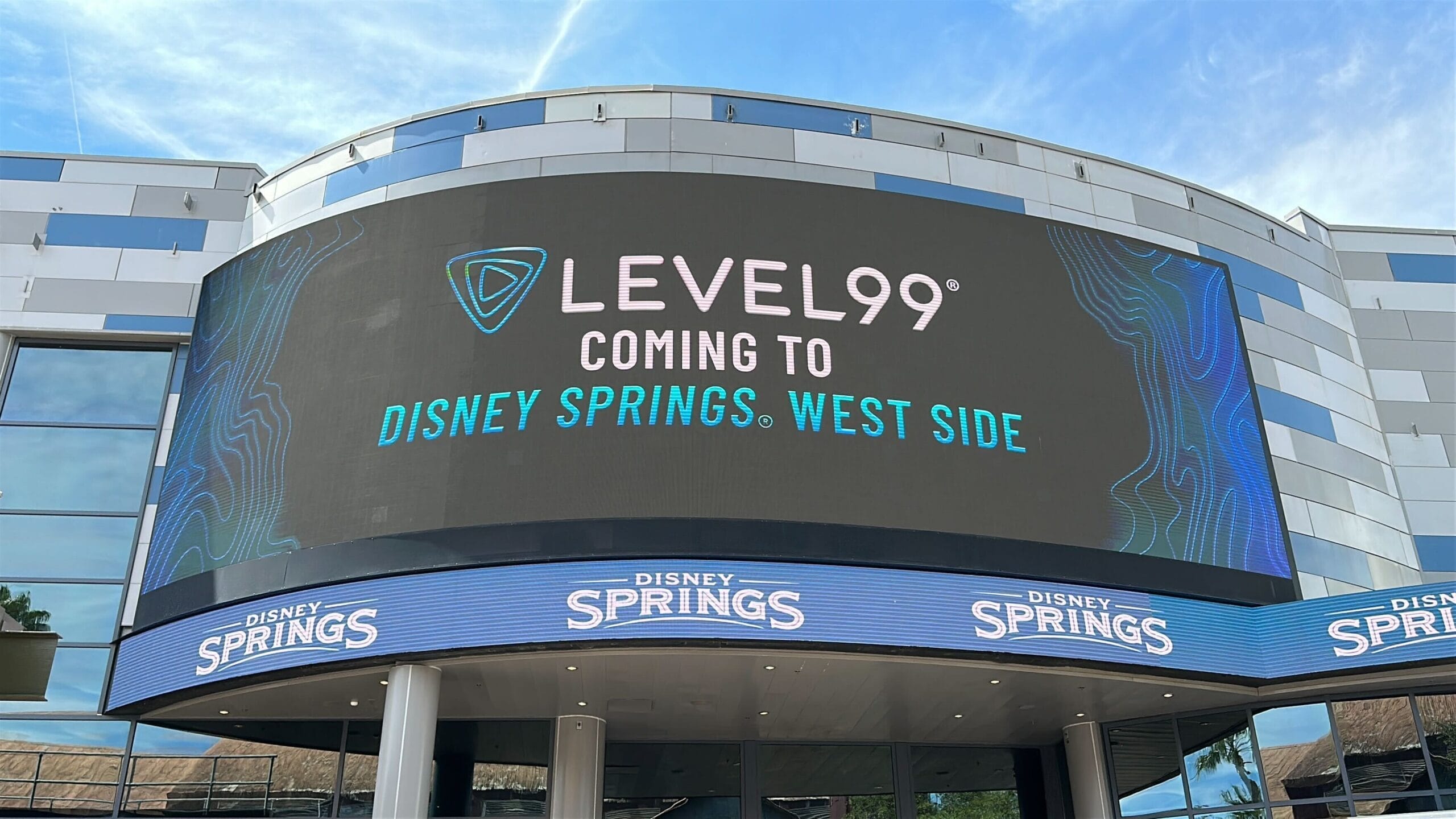 A modern facade at Disney Springs displays a digital sign: "Level99 Coming to Disney Springs West Side."