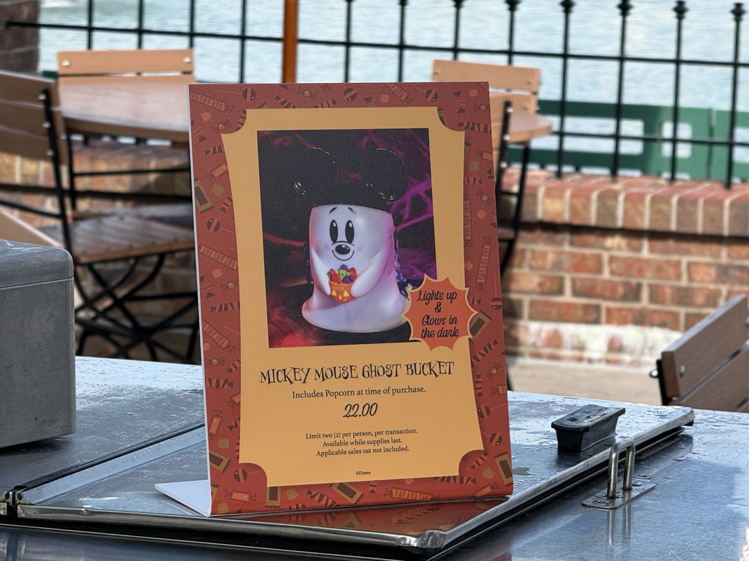 At Disney World, a table sign advertises the Mickey Mouse Ghost Popcorn Bucket for $22 on an outdoor counter.