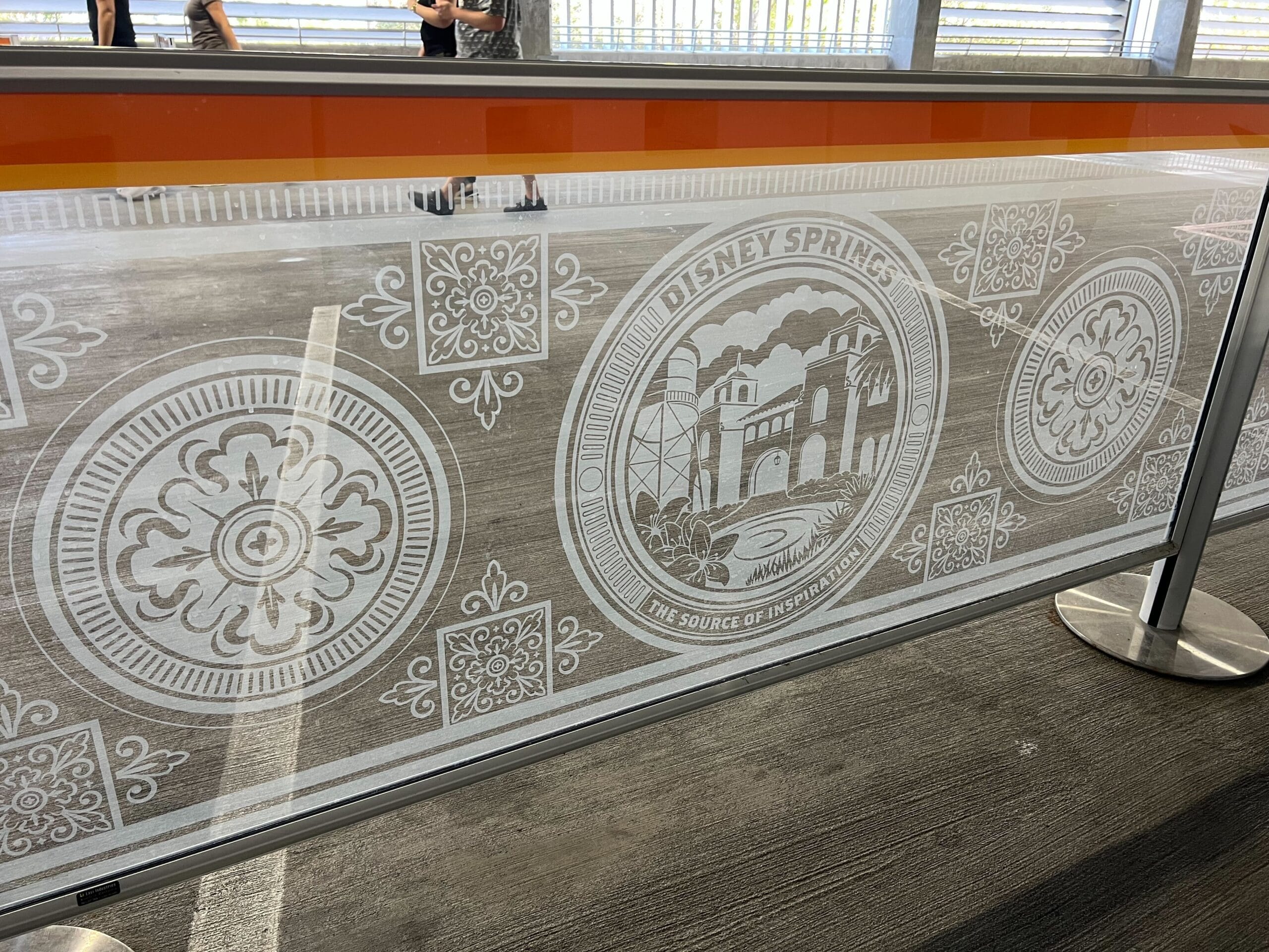 Glass barrier featuring white etched designs and a Disney Springs logo in a parking garage, no castle like those at Disney parks visible.