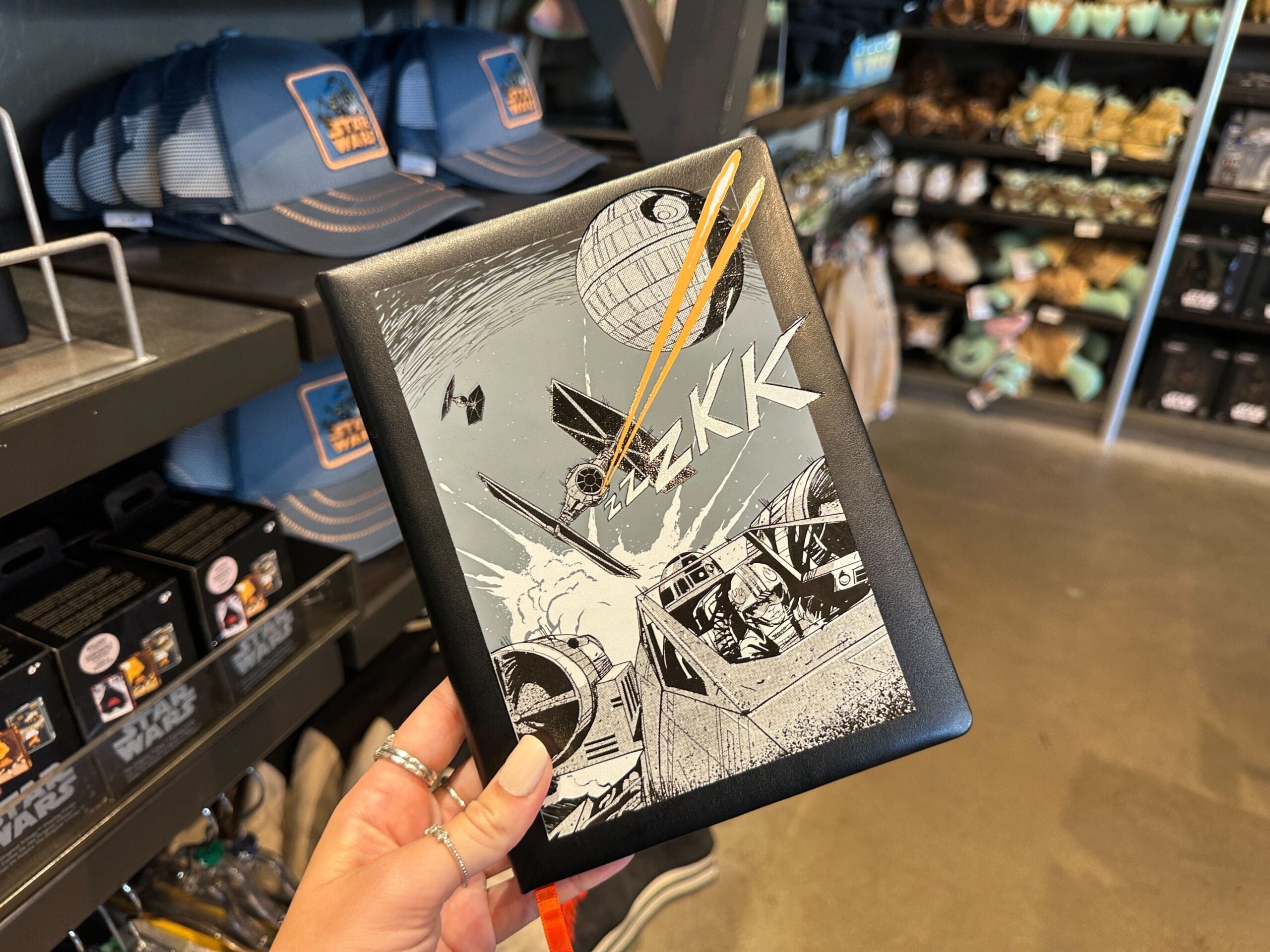 A hand displays a Star Wars notebook featuring Death Star and X-wing art, found at a Disney World shop near Cinderella Castle.