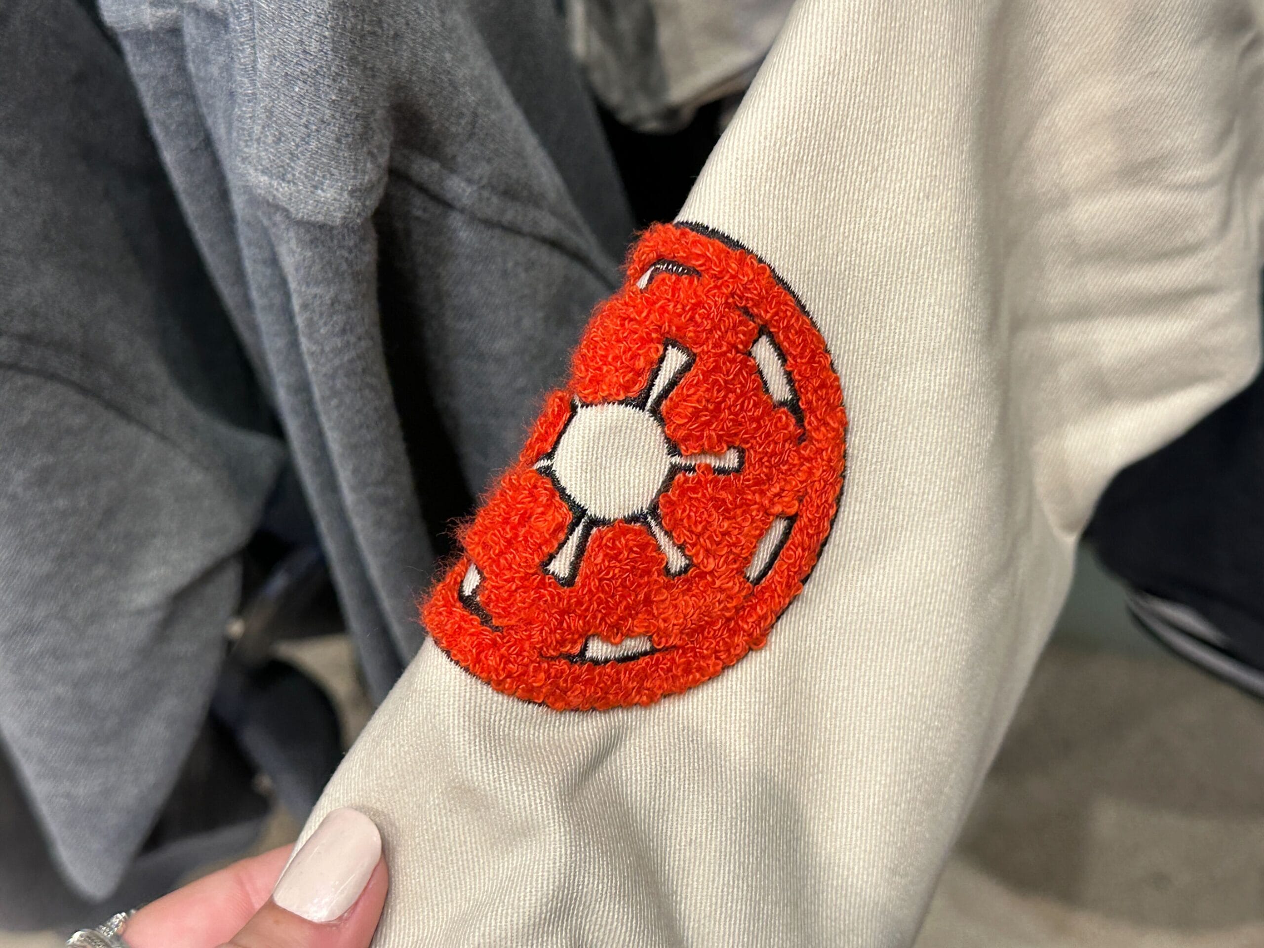 A hand holds fabric with an orange embroidered donut-like patch, great for Star Wars gear sold near Disney castle-themed shops.