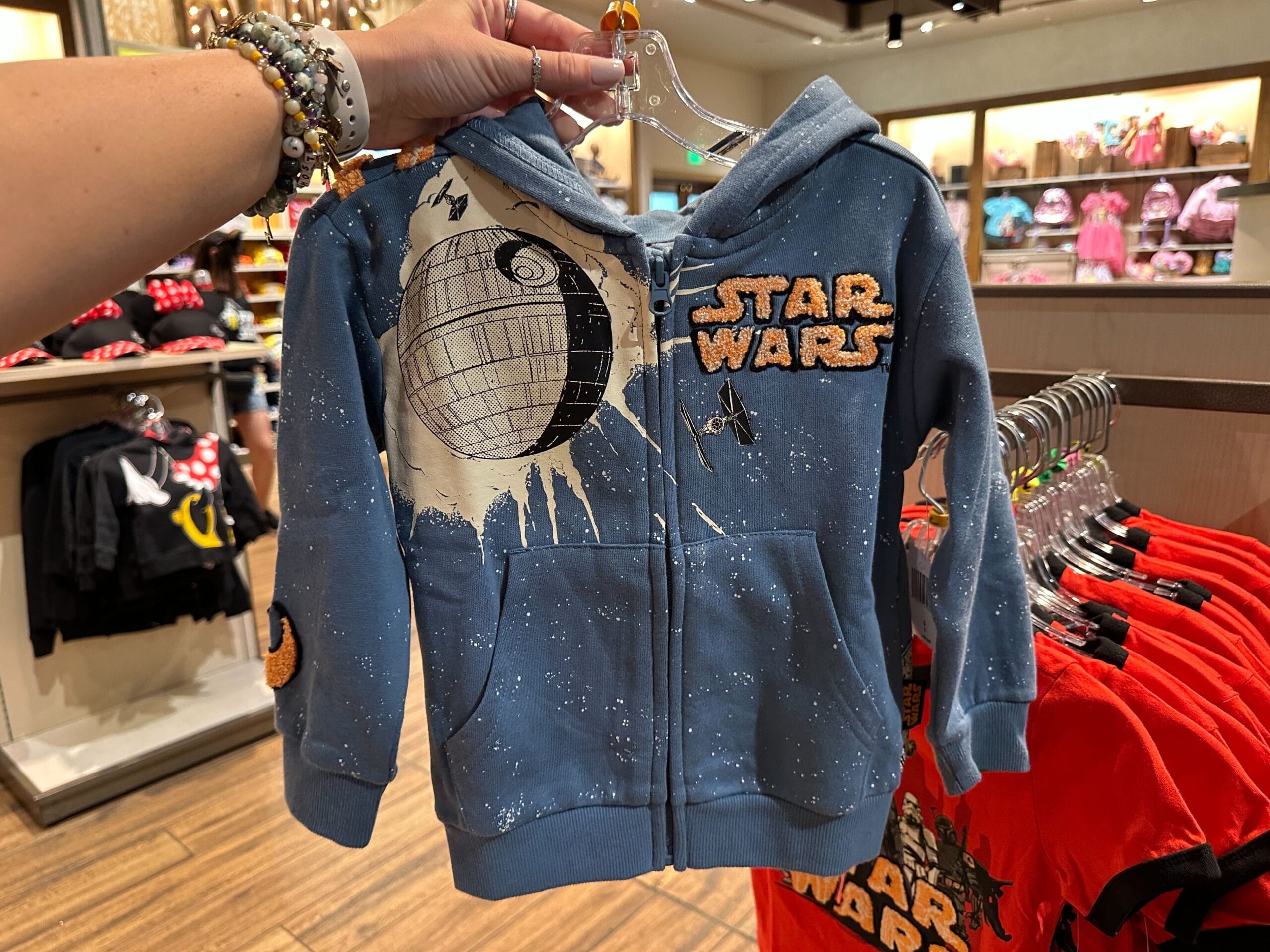 Blue Star Wars kid's hoodie with Death Star and X-wing, among Disney World Star Wars gear—no castle like Magic Kingdom’s visible.