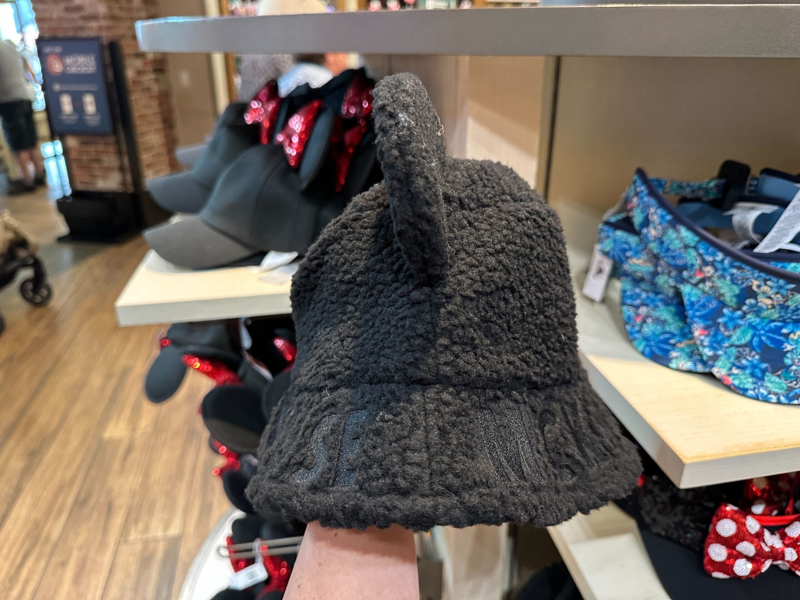 A fuzzy black bucket hat with bear ears, reminiscent of Disney’s Mickey Mouse Sherpa hats, is displayed in a park gift shop.