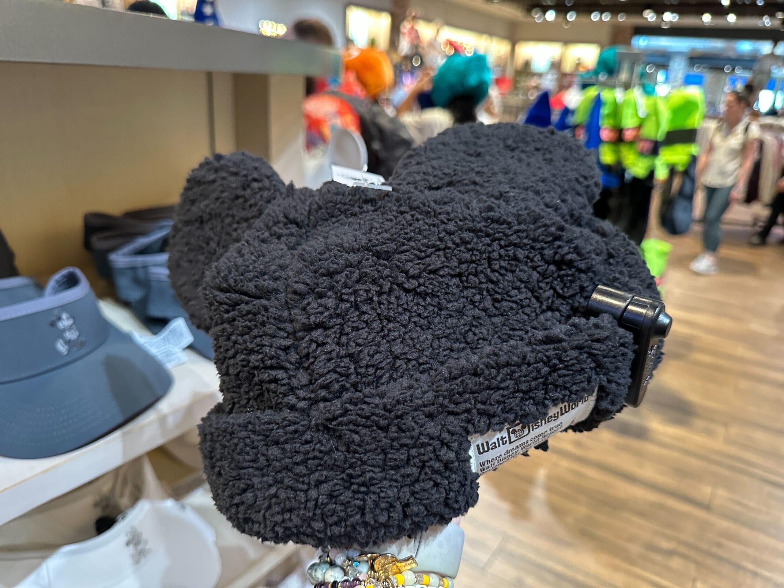 A cozy black Mickey Mouse Sherpa Hat for winter, featured in a bustling Disney World shop near Cinderella Castle.
