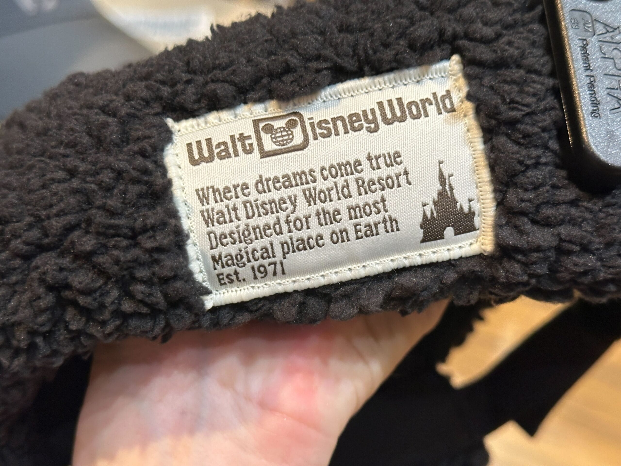 A clothing label says "Disney World, Where dreams come true, Est. 1971," hinting at cozy Mickey Mouse Sherpa Hats. No castle shown.