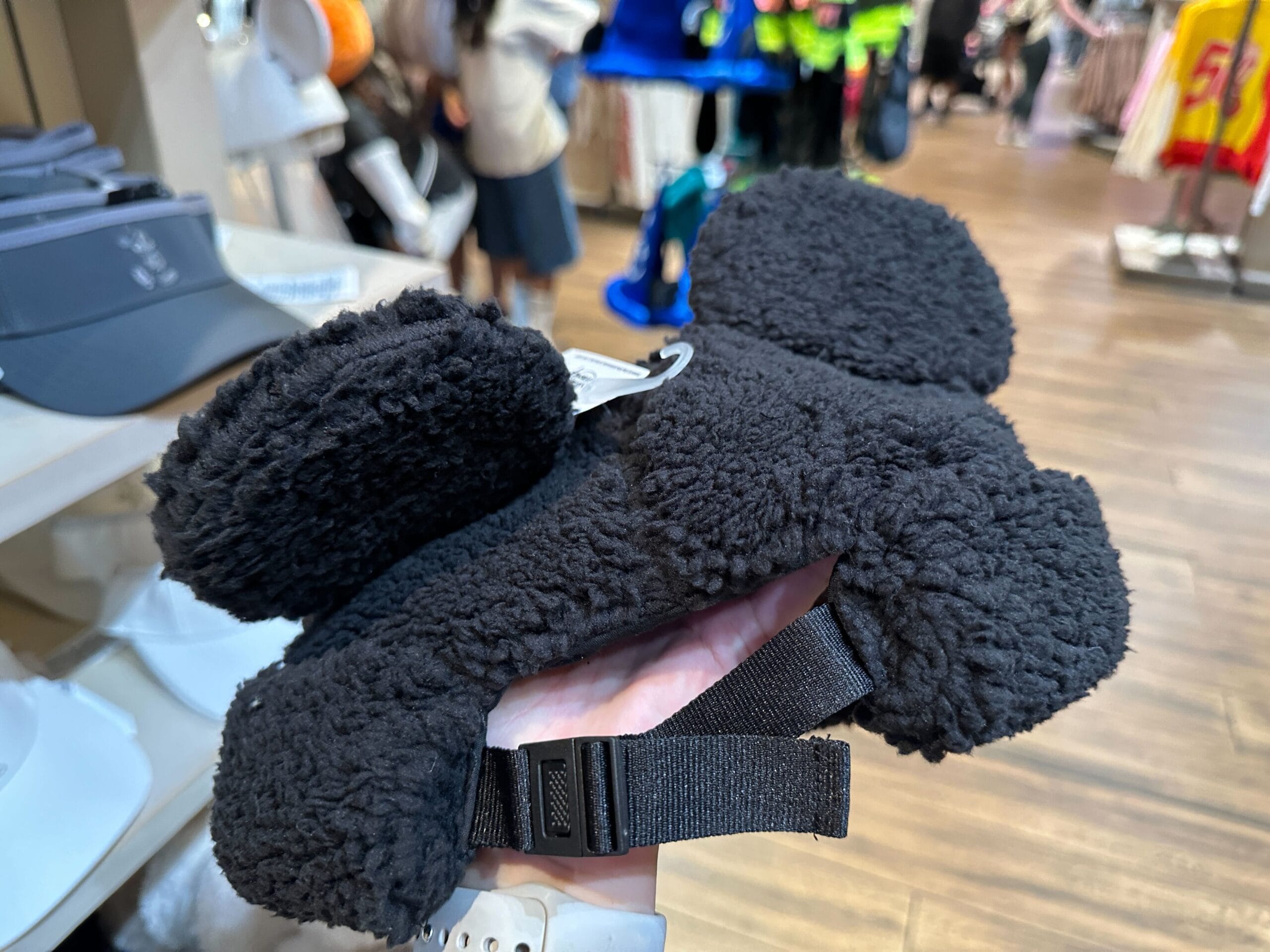 A hand holds a black furry hat, cozy for winter days or exploring Disney Parks—ideal gear whether at Disneyland or Walt Disney World.