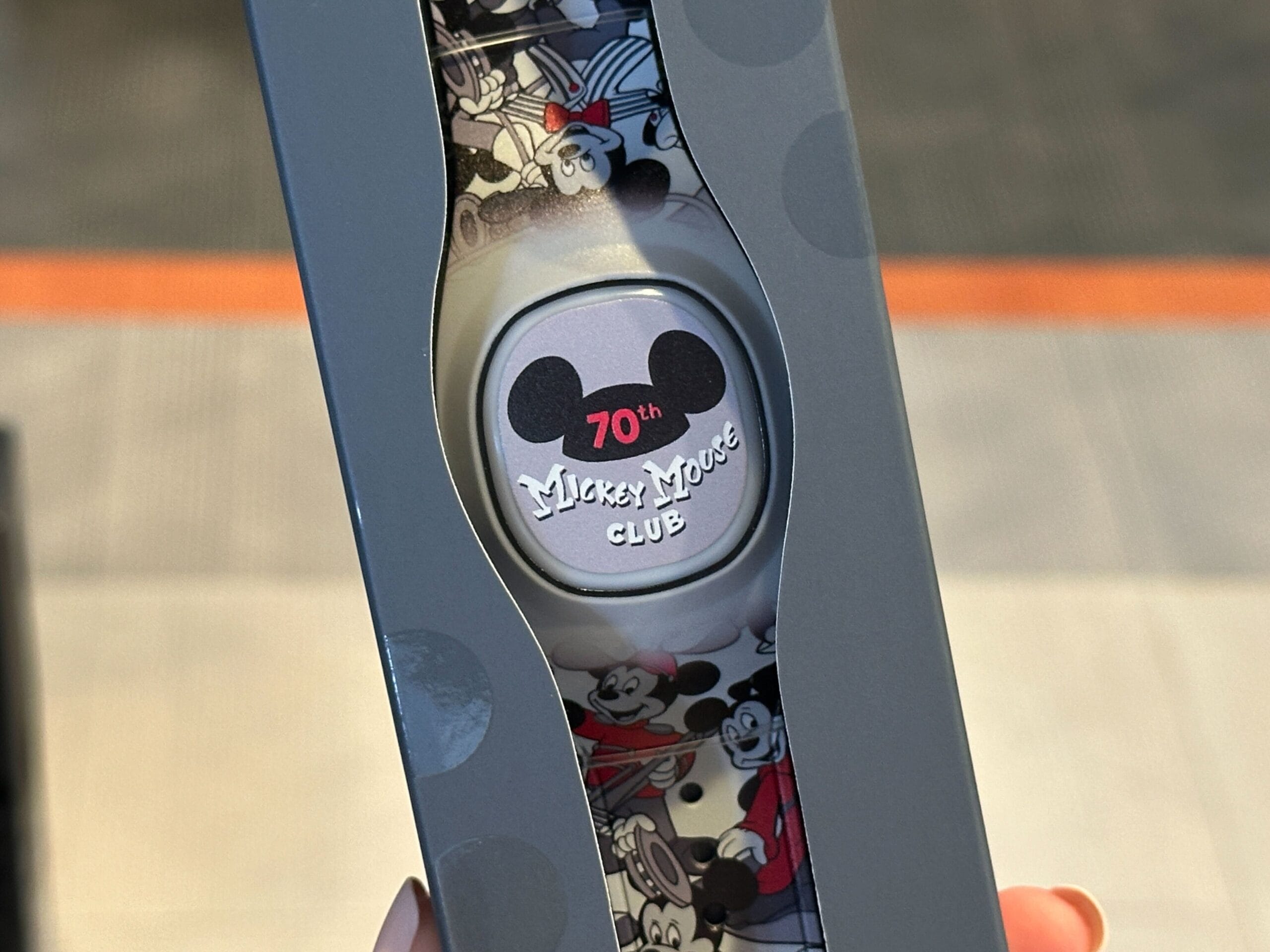 Close-up of a "Mickey Mouse Club 70th" MagicBand+ with Mickey Mouse designs, held in a hand.