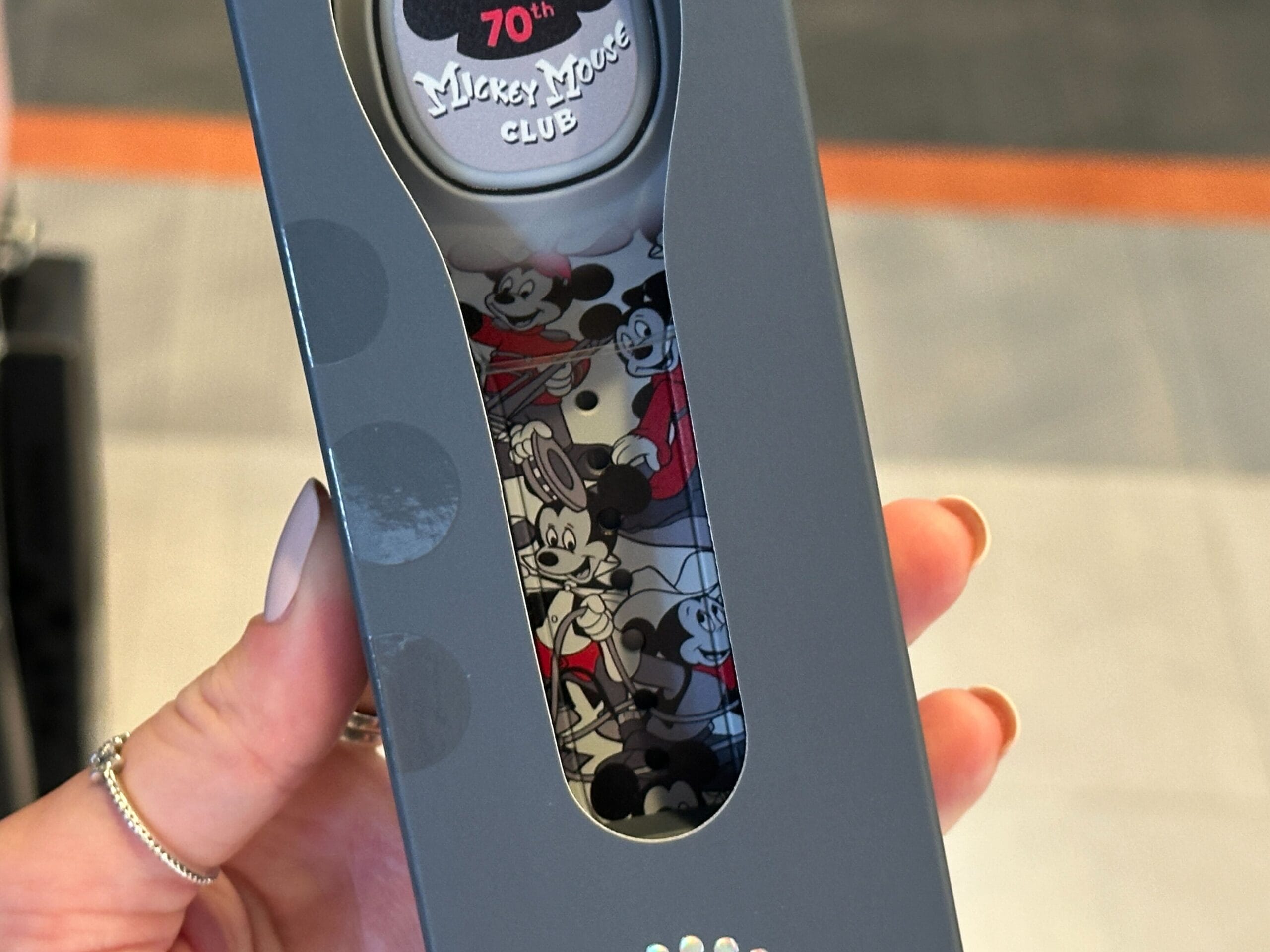 Hand holding a boxed watch celebrating the 70th Mickey Mouse Club anniversary, featuring MagicBand+ and Mickey illustrations.