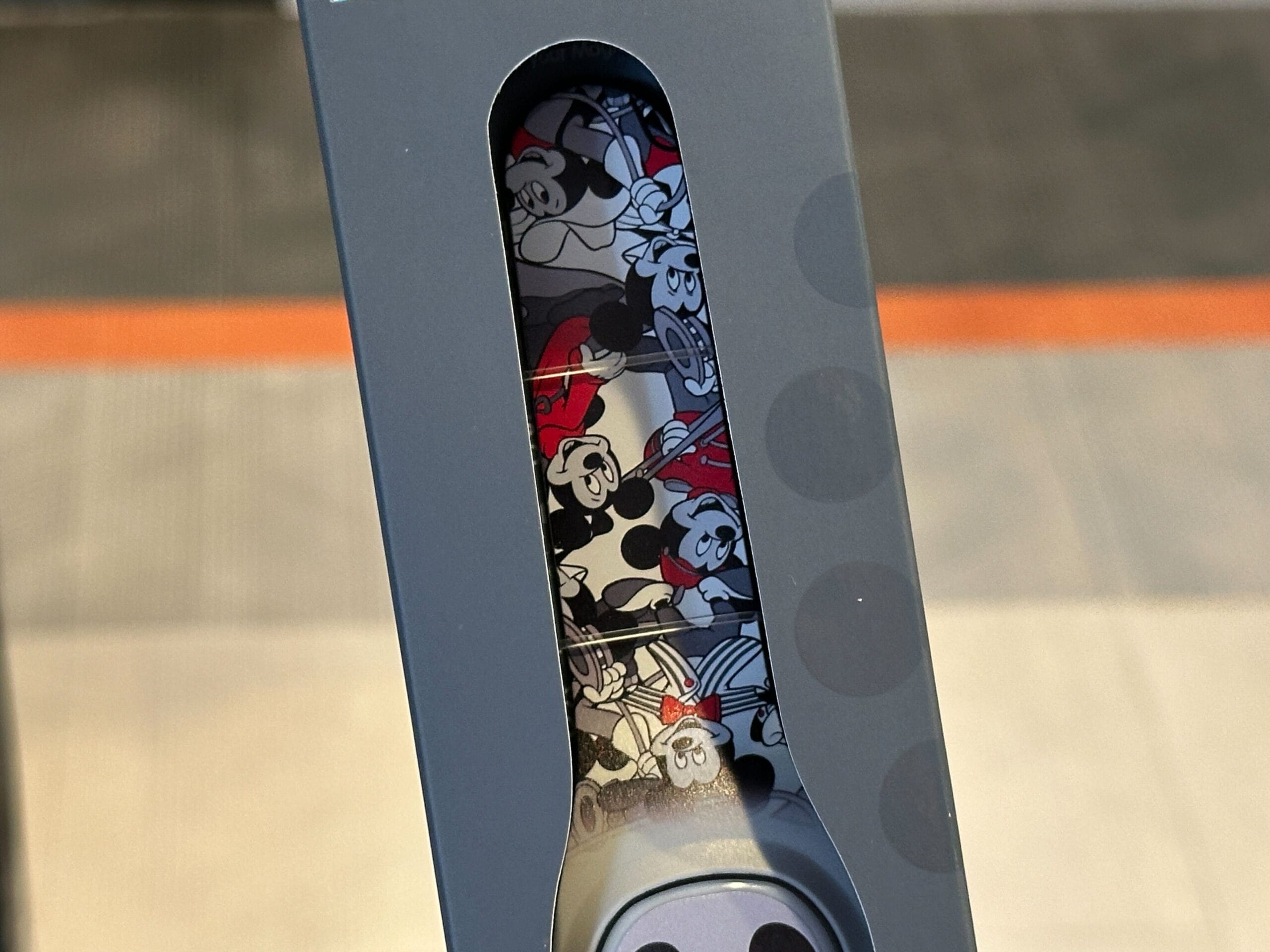 A close-up of a box with a window showing a MagicBand+ featuring cartoon mouse faces in black, white, and red.