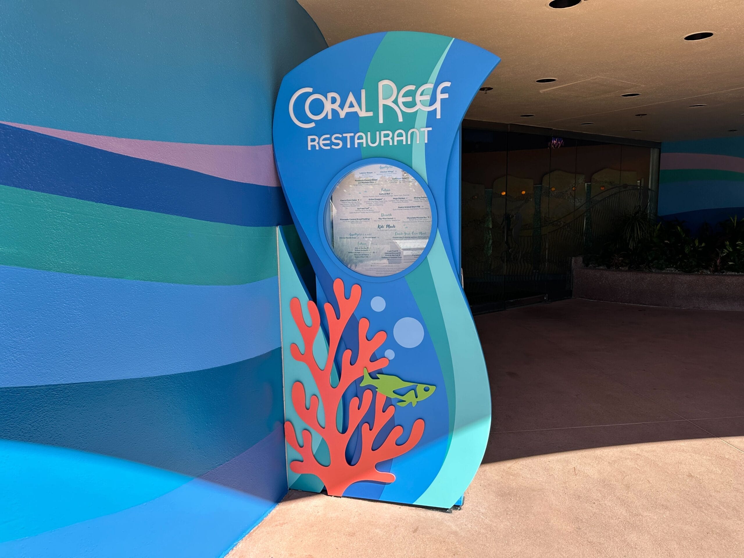 Bright blue Coral Reef Restaurant exterior menu board sign with fish and coral accents at EPCOT.