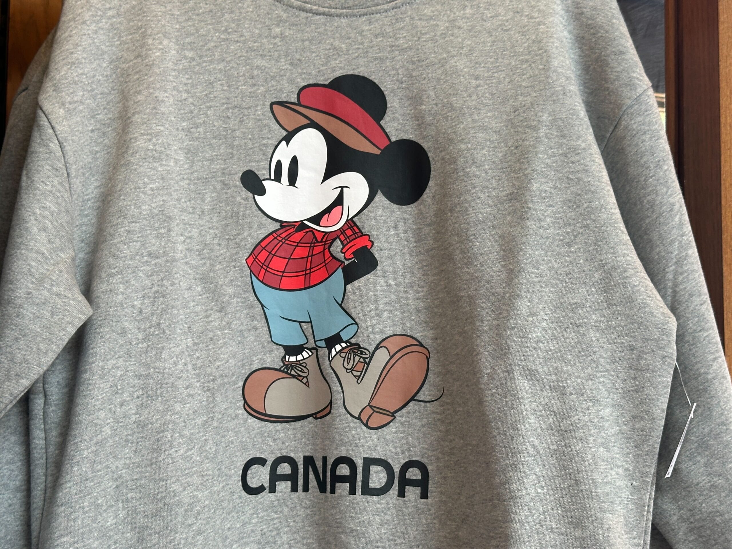 Gray sweatshirt featuring Mickey Mouse in plaid, boots, and hat over "CANADA"—perfect for EPCOT World Showcase fans.