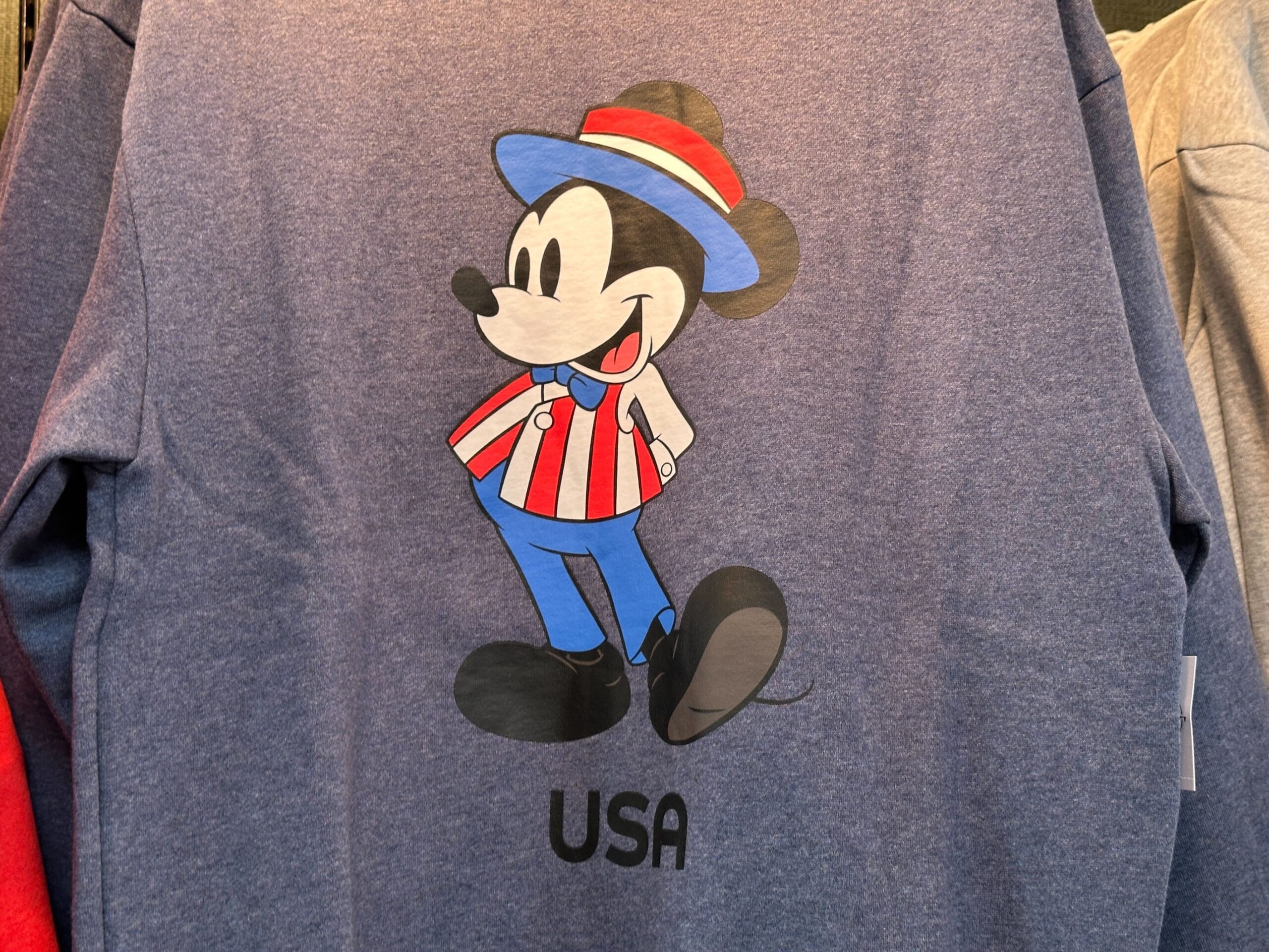 Cartoon Mickey Mouse in red, white, and blue EPCOT outfit with "USA" text on a blue shirt.