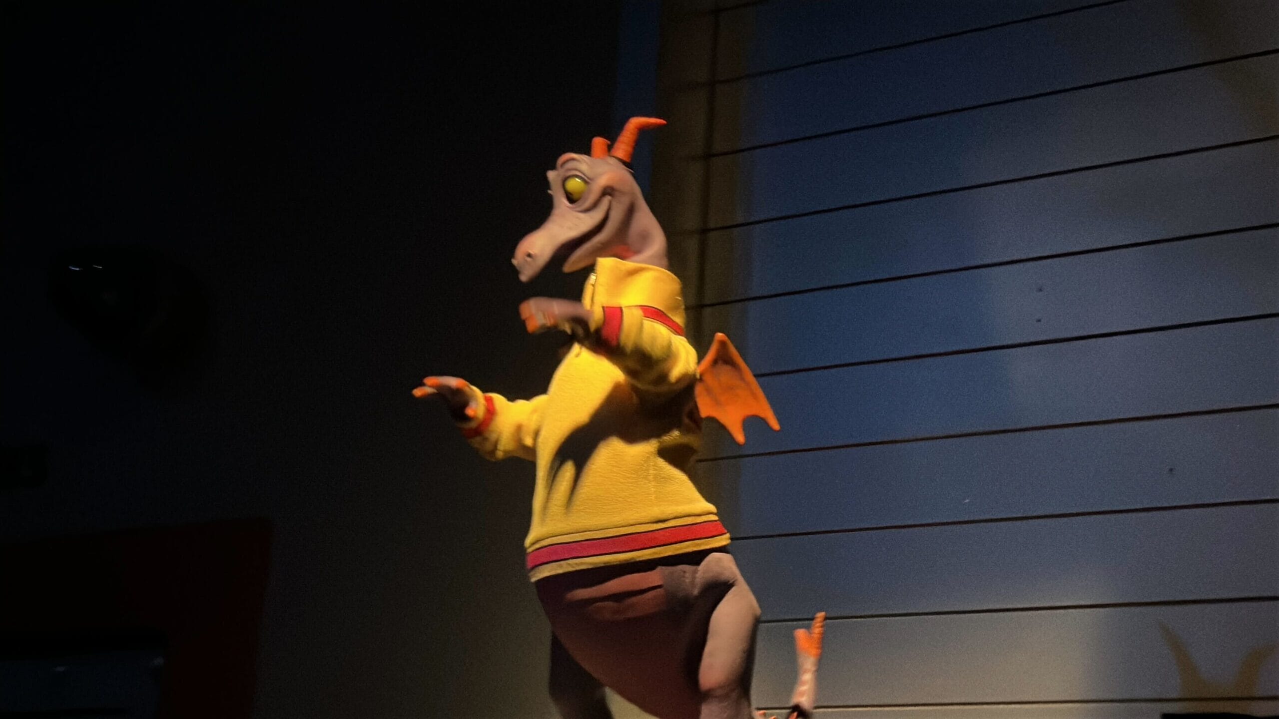 Figment, the small purple dragon in a yellow sweater, stands excitedly with arms up, ready at EPCOT’s Journey Into Imagination.