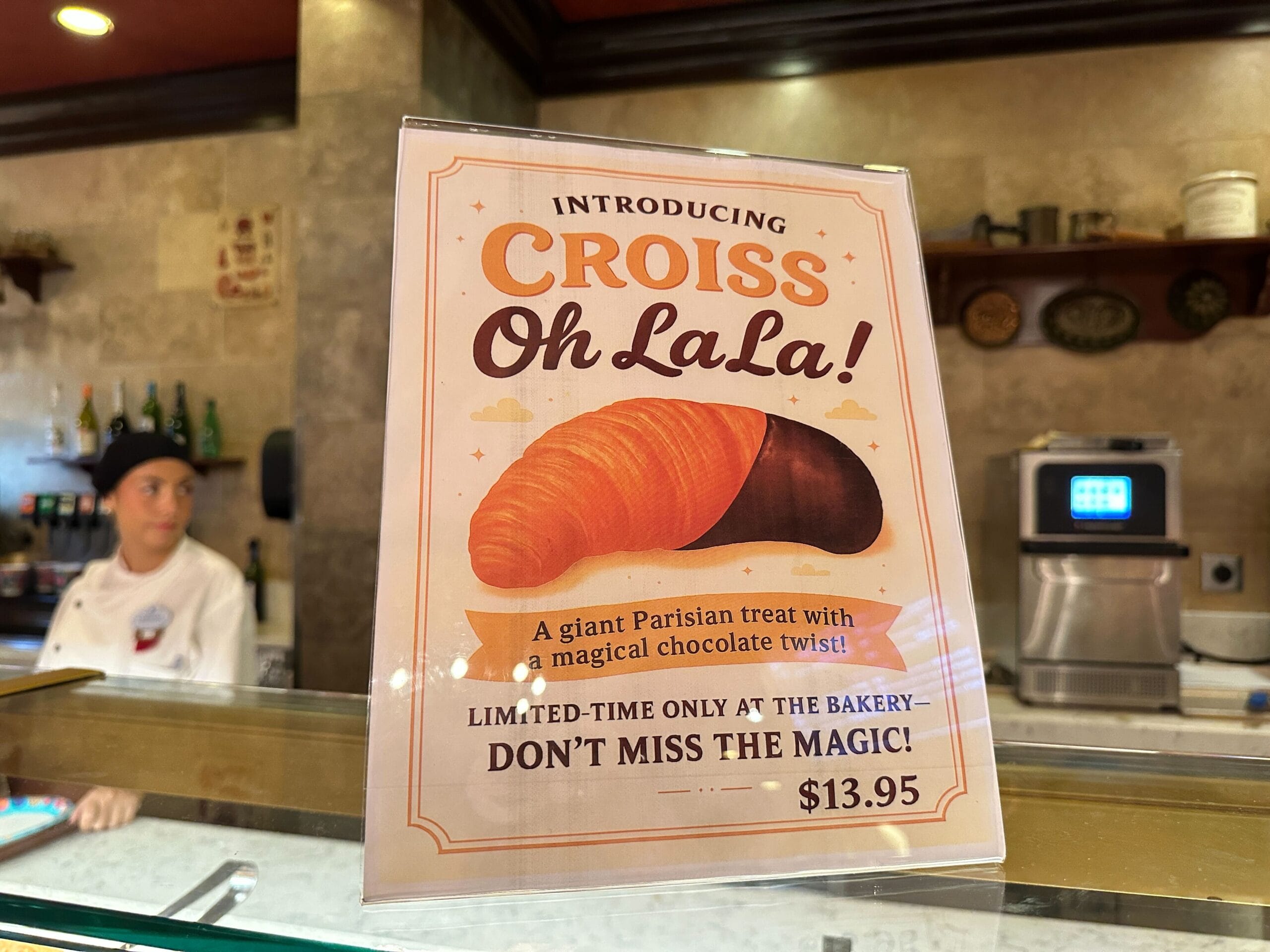A bakery sign at EPCOT advertises a half-chocolate, half-plain Chocolate Twist Croissant called "Croiss Oh LaLa!" for $13.95.