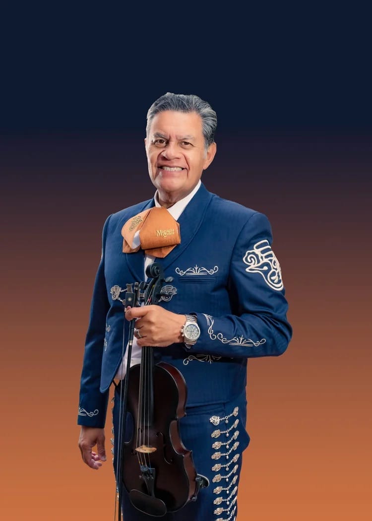 A smiling Mariachi Cobre violinist in a blue suit poses against an orange and navy gradient, as seen at EPCOT in Walt Disney World.
