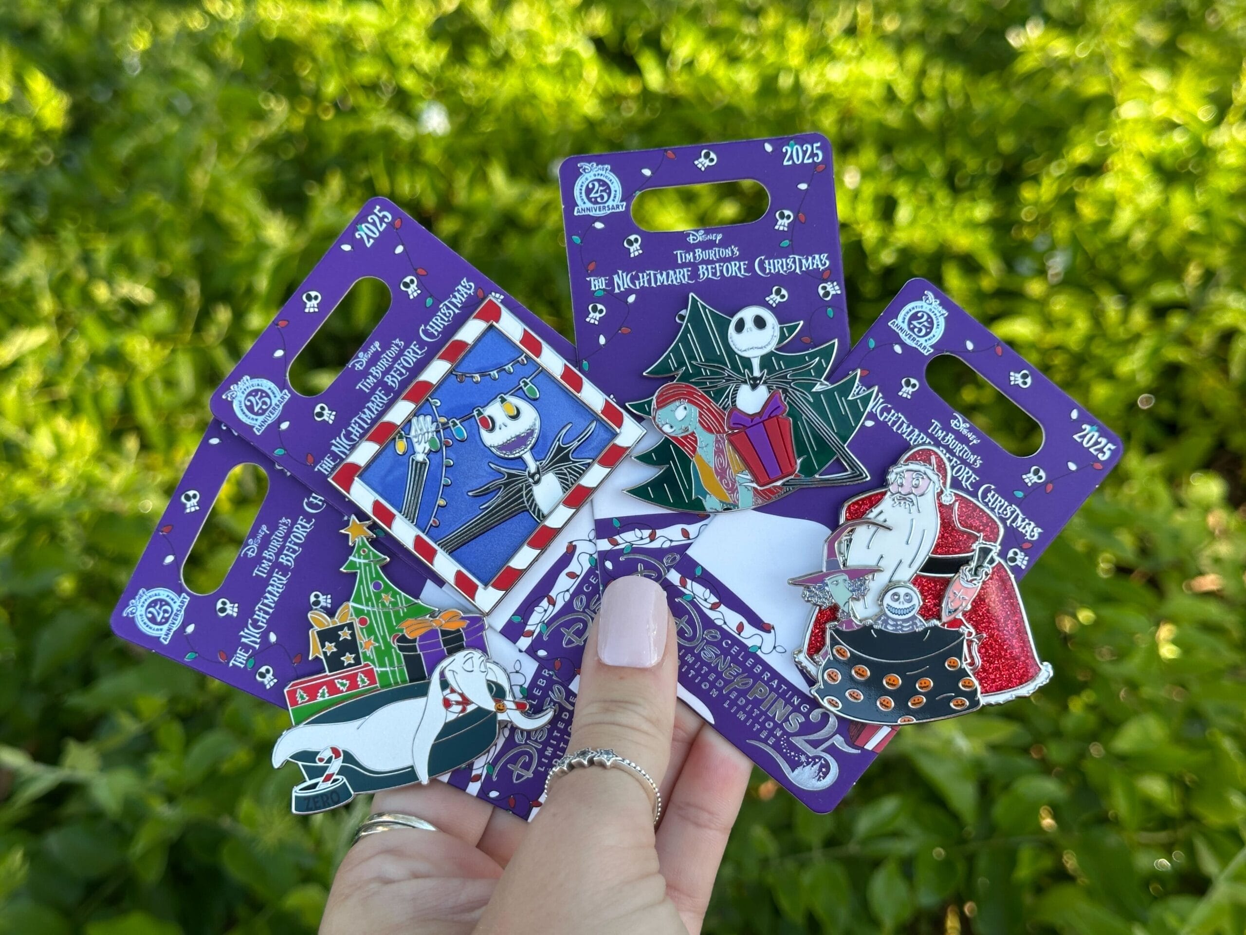 A hand displays four Disneyland Nightmare Before Christmas 2025 pins featuring Zero, Jack Skellington, Sally, Santa, and Lock, Shock, and Barrel.