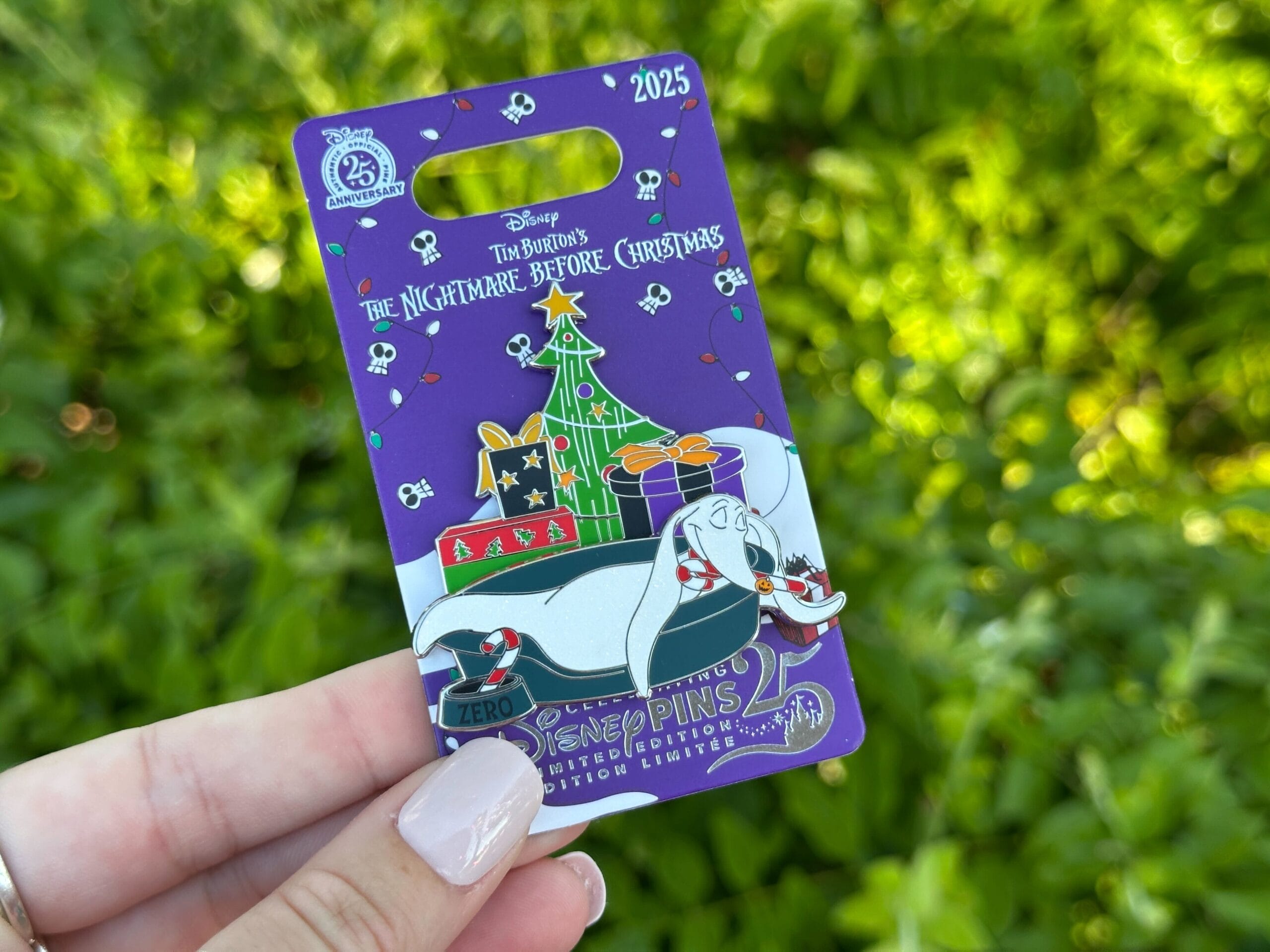 A hand holds a 2025 Disney World pin with Zero the ghost dog and a Christmas tree, exclusive to the park, no castle in view.