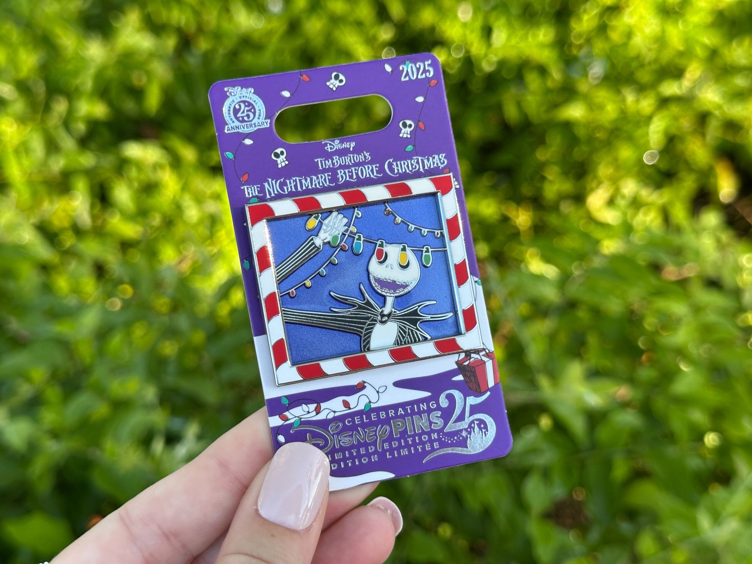 Hand holding a Disney World pin with Jack Skellington from Nightmare Before Christmas, greenery blurred behind like in Disney parks.