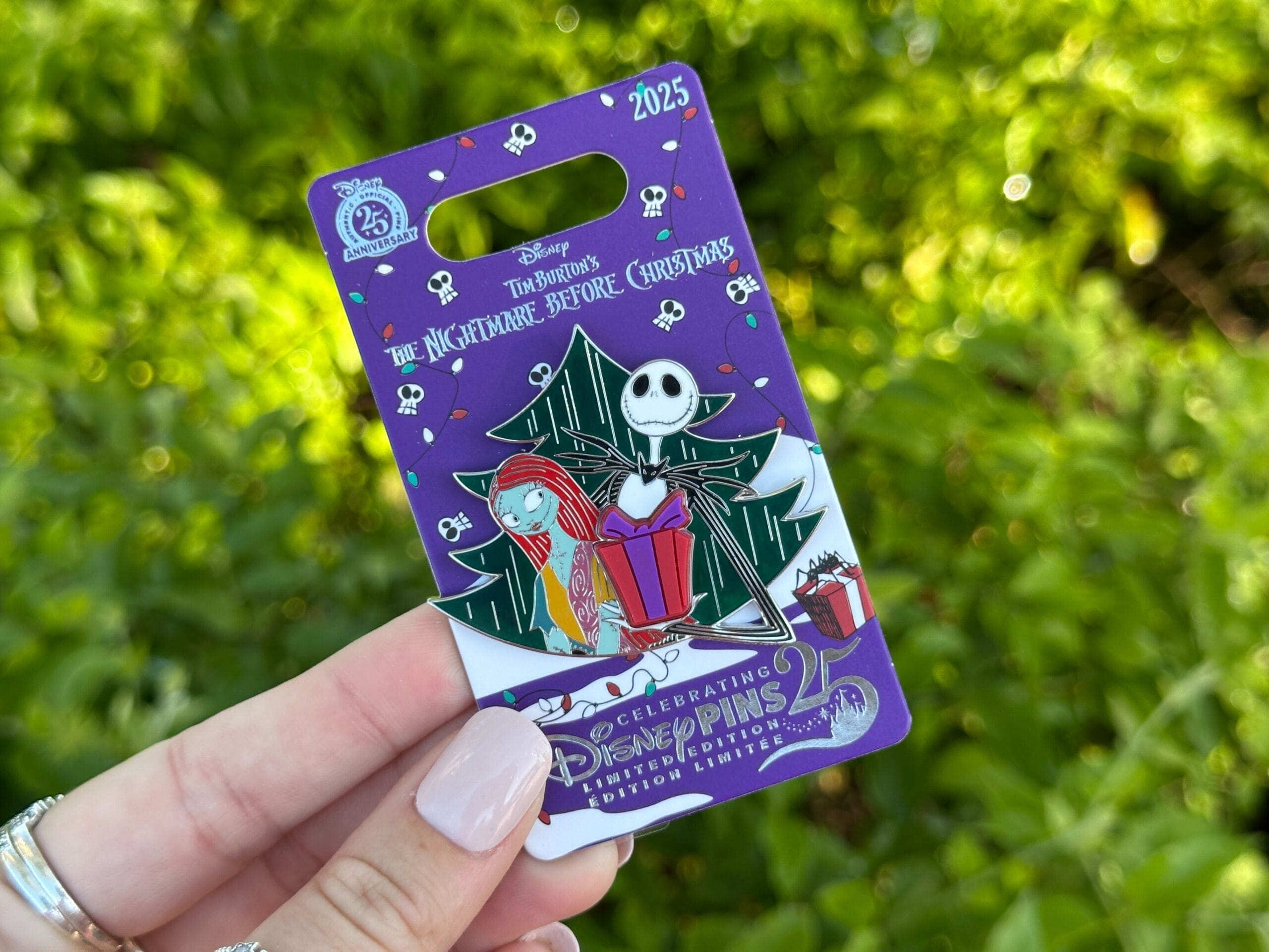 A hand holds a Walt Disney World pin: Nightmare Before Christmas 2025 with Jack and Sally by a Christmas tree, no castle depicted.