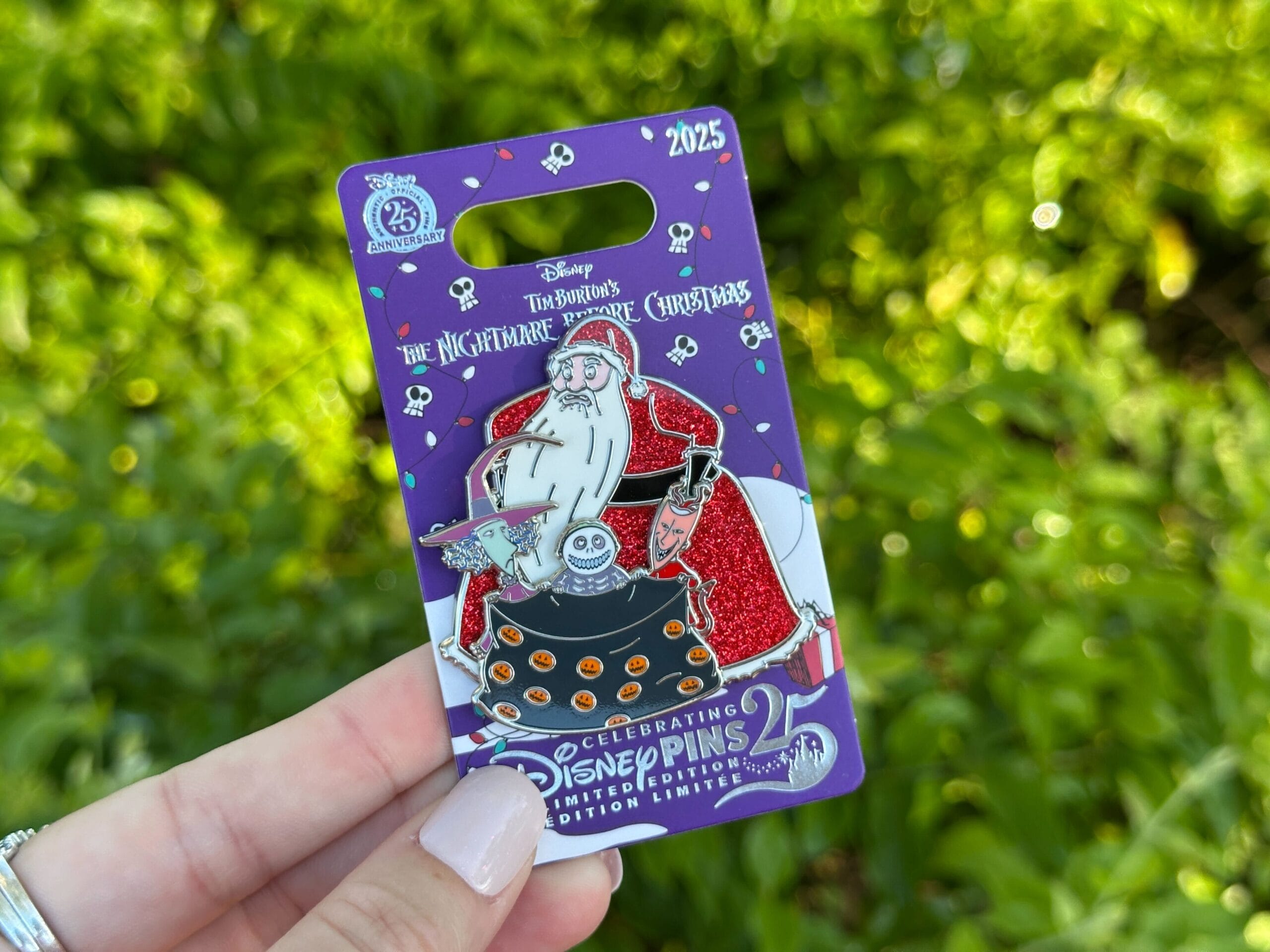 A hand displays a 2025 Disney World pin of Santa Jack and Zero from Nightmare Before Christmas, greenery in the background.