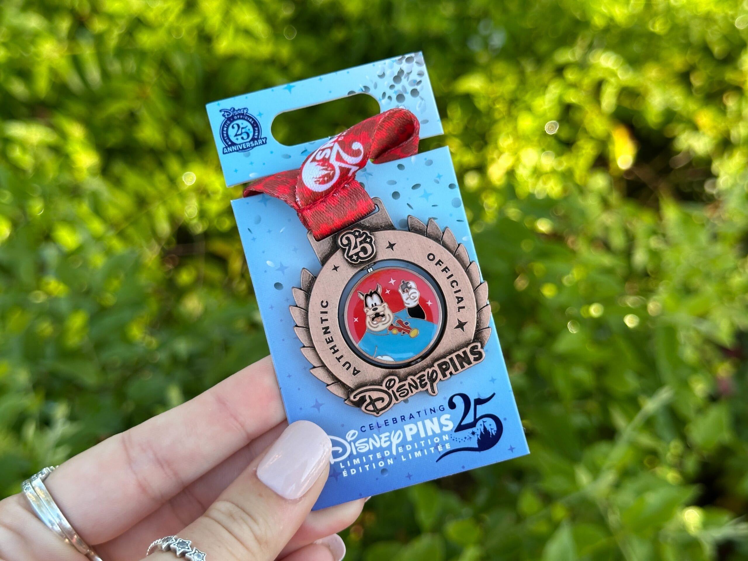 A hand holds a Disney Pins 25th anniversary pin at Disney World, ideal for Pin Tuesday—no castle like the ones in global parks visible.